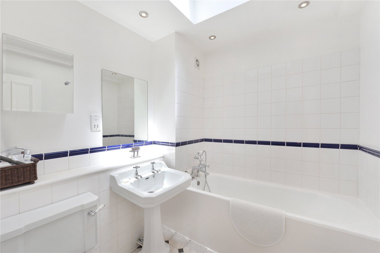 Bright white bathroom with modern fixtures and blue tiled accents, featuring a bathtub and pedestal sink.
