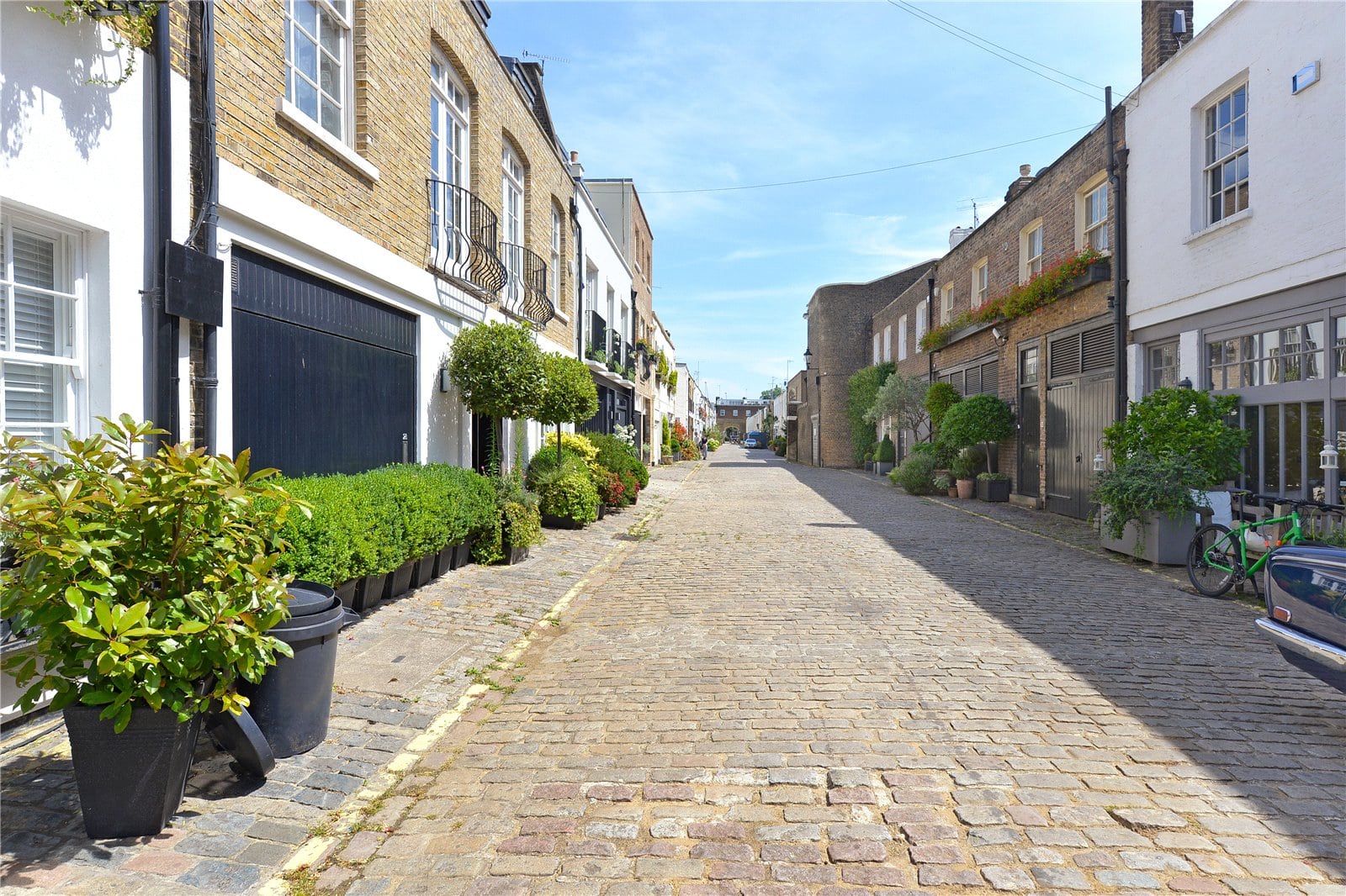 Charming cobbled street with colourful houses and lush greenery in London’s historic neighbourhood.