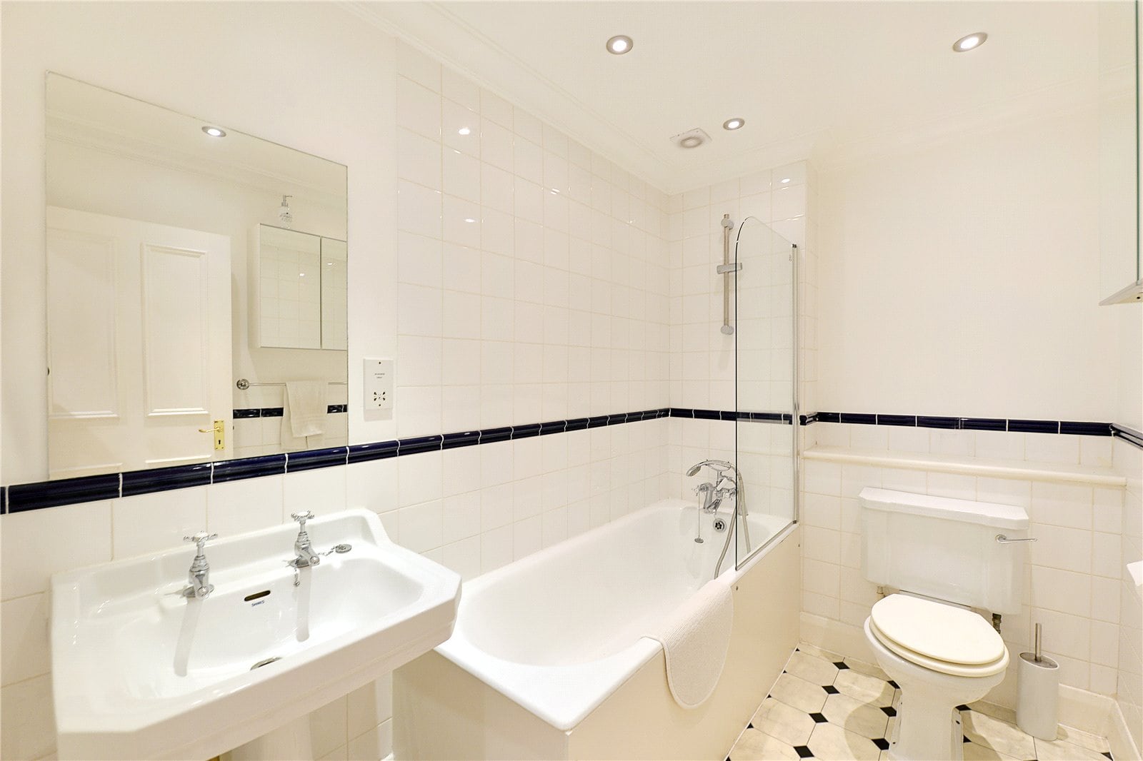 Bright white bathroom with bathtub, shower, vintage sink, and toilet, featuring black tile accents and recessed ceiling lighting.