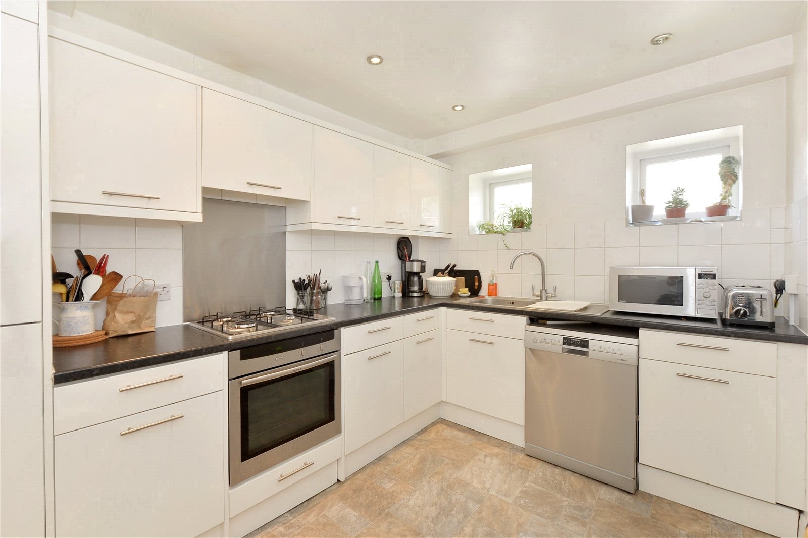 Modern white kitchen with black countertops and stainless steel appliances, including oven, microwave, and dishwasher.