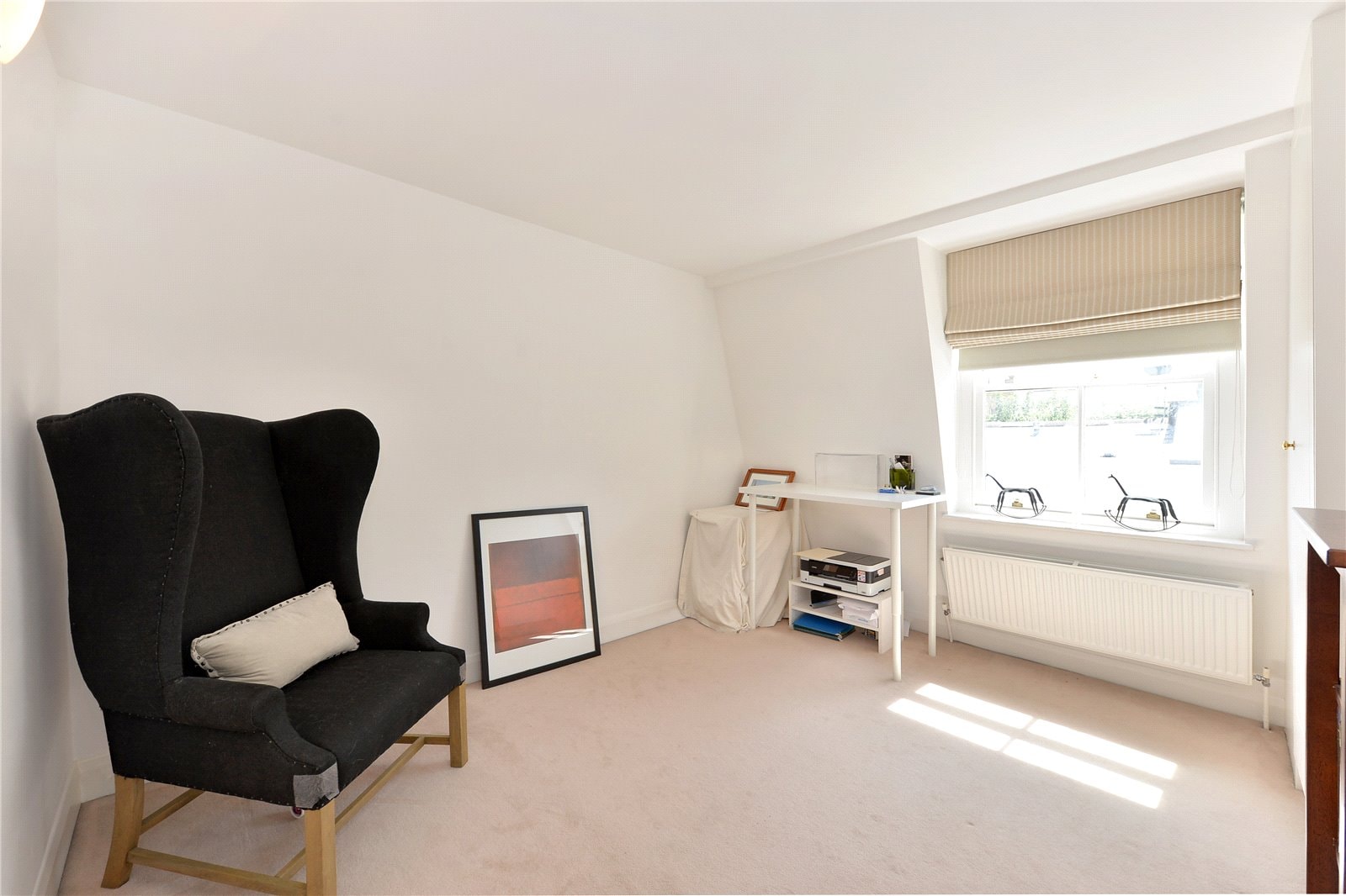 Modern empty bedroom with large window, beige carpet, and black high-back armchair for sale in London.