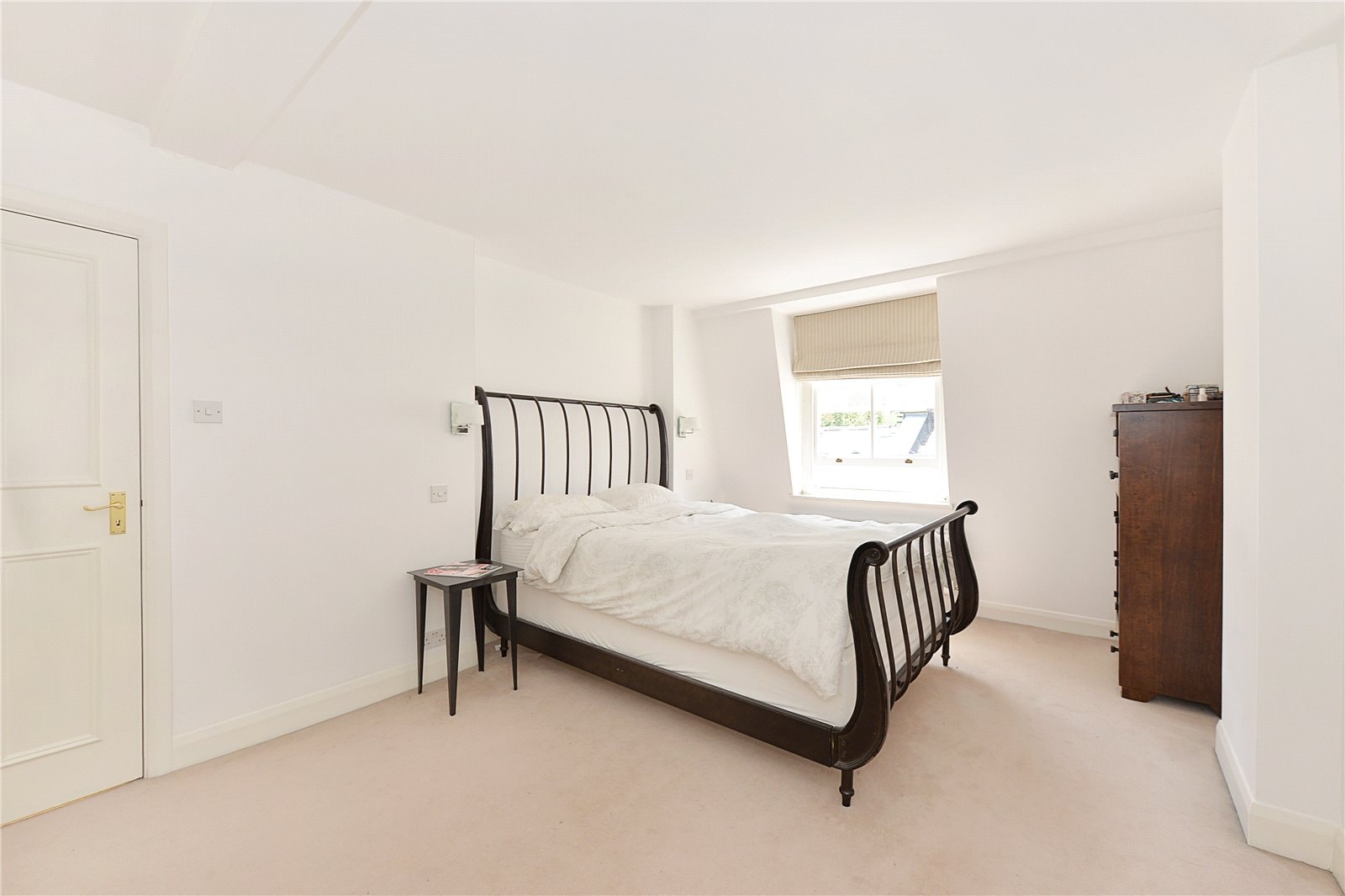 Stone-walled bedroom with black metal bed frame, bedside table, and wooden dresser.