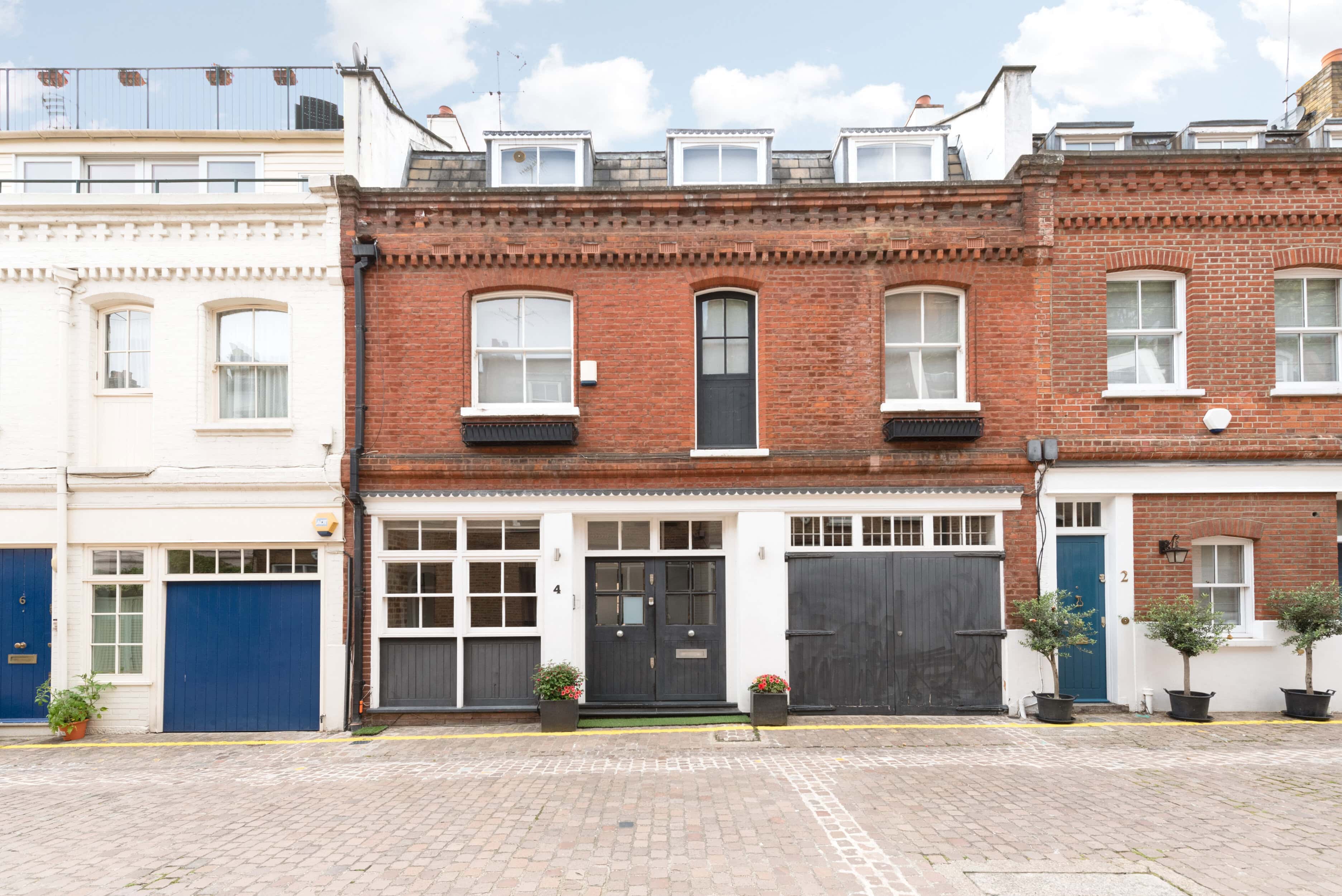 Red brick townhouse in Adam and Eve Mews in Kensington with black door and white window frames.