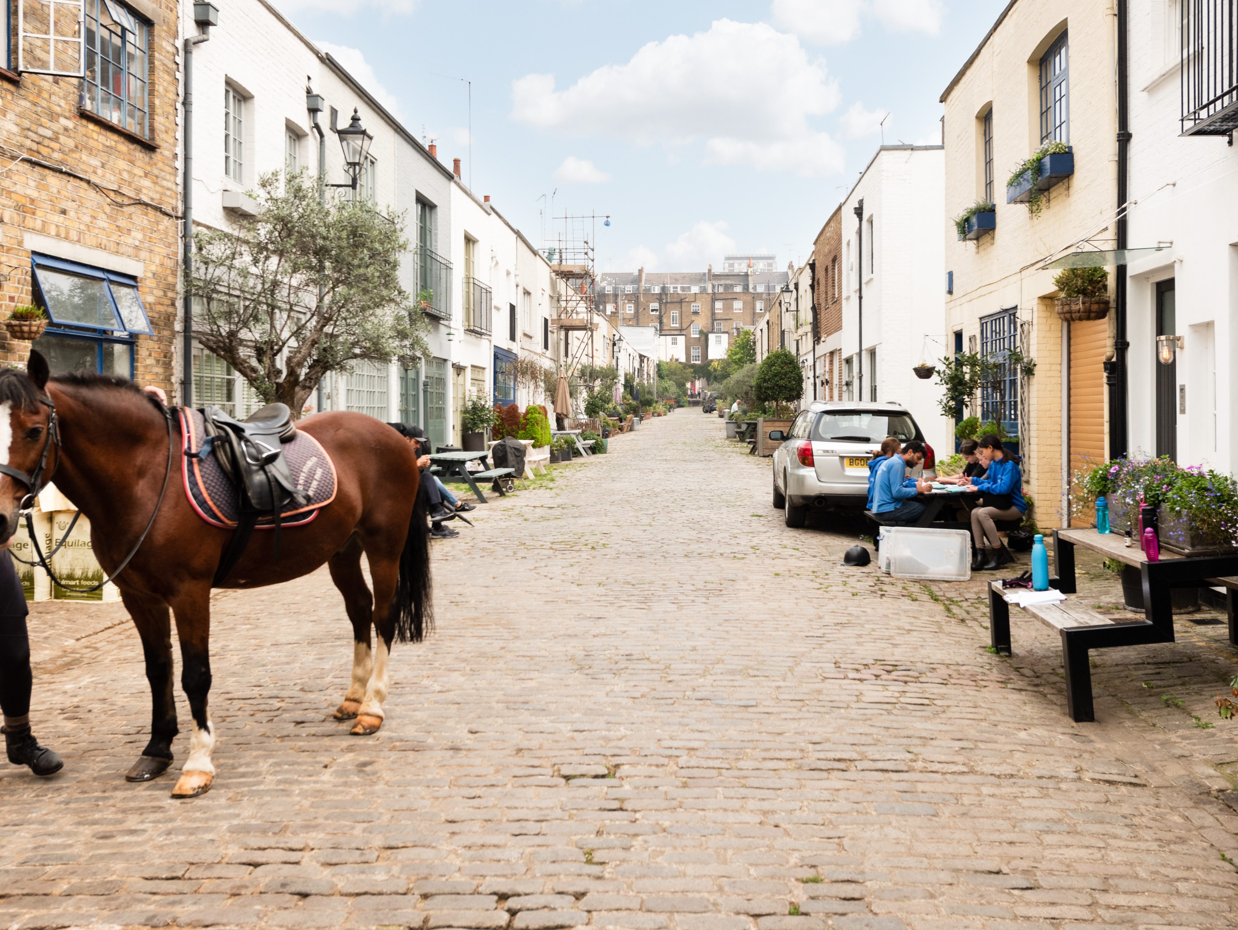 Charming cobbled street in Bathurst Mews, Bayswater with horse and people sitting outside.