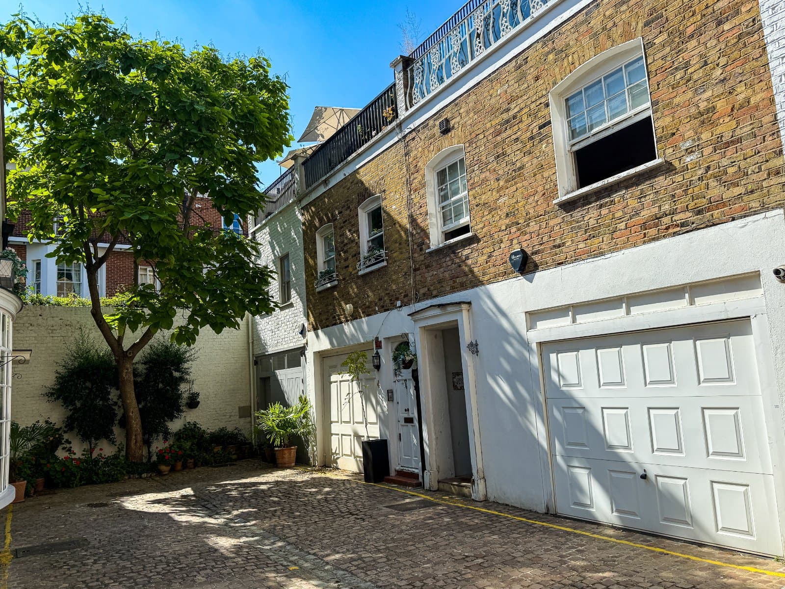 Charming townhouse with a cobbled driveway and lush greenery in a desirable London neighbourhood.