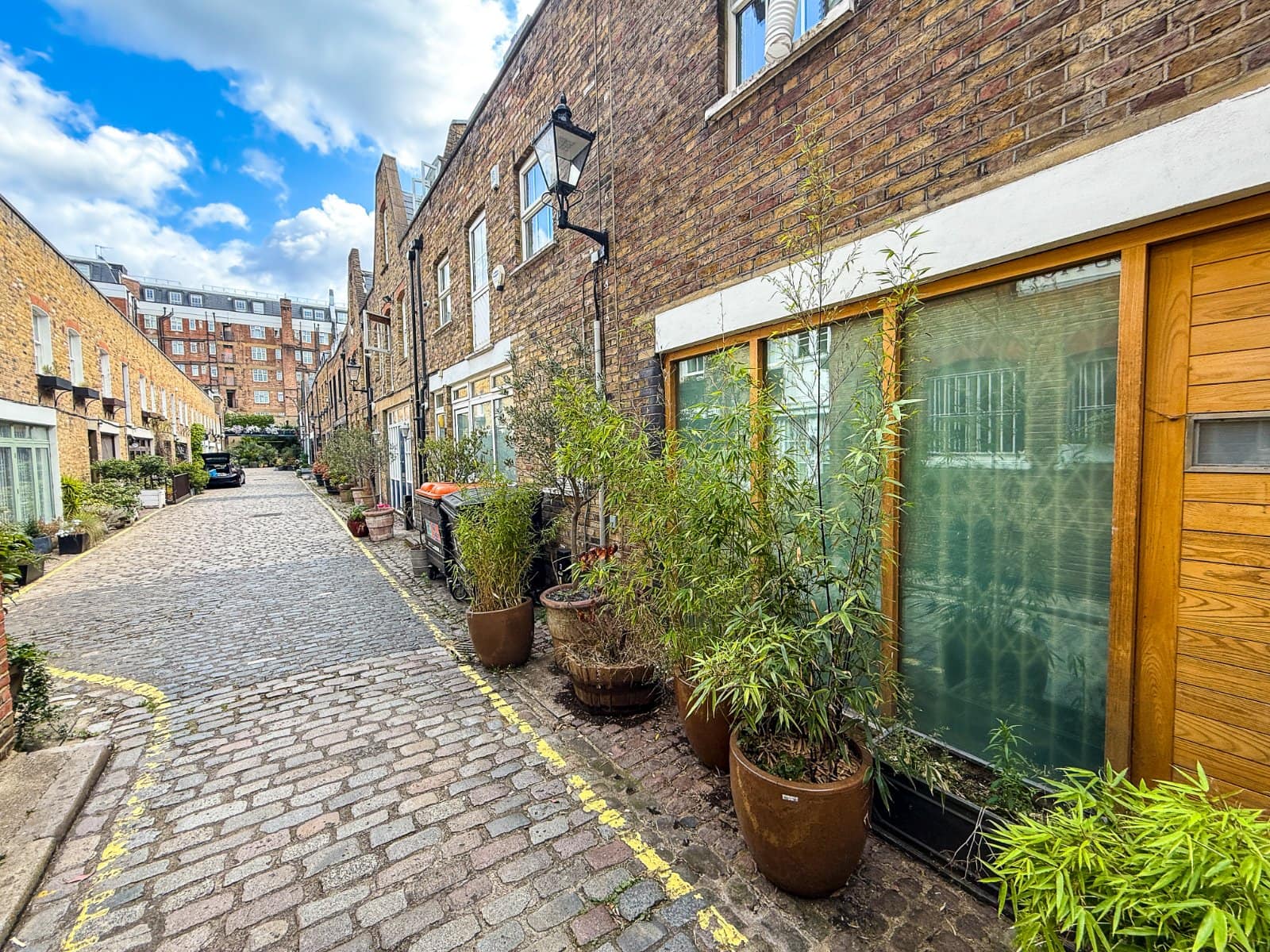 Charming cobbled street with residential buildings and potted plants, showcasing London’s historic urban character.
