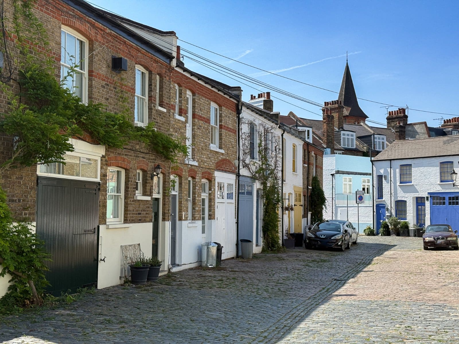 Charming colourful cobbled street with traditional European-style houses and parked cars.