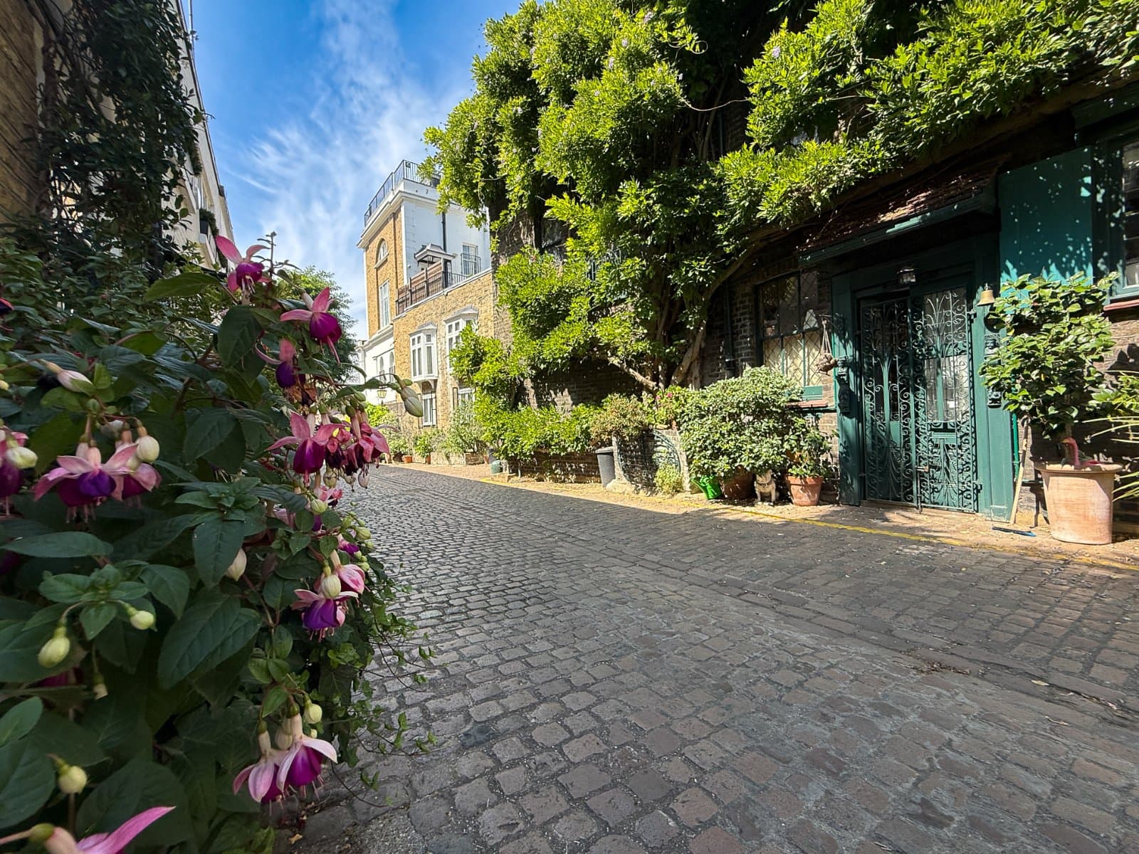 Cobblestone street with charming historic buildings and lush greenery in London.