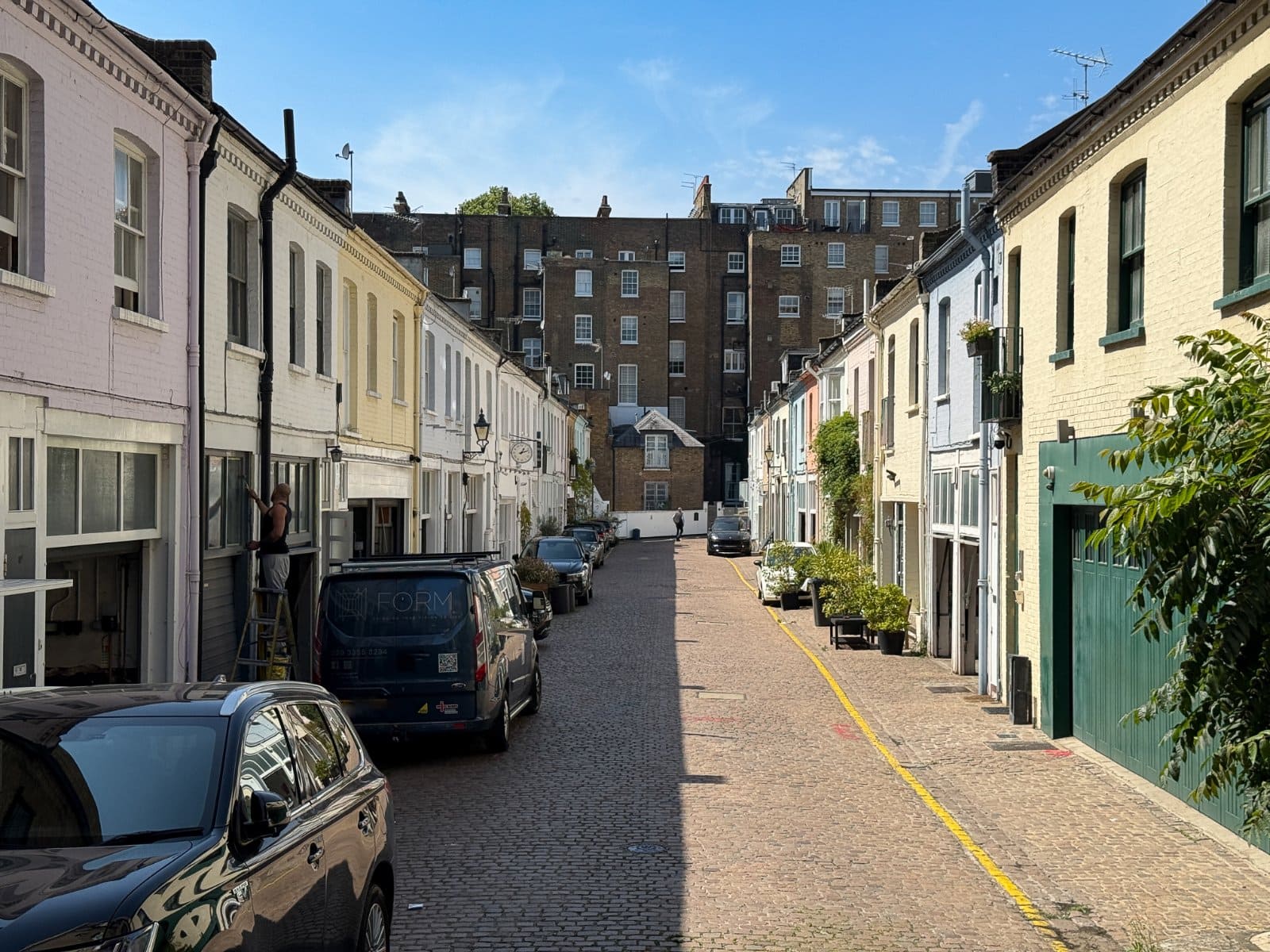 Elegant row of colourful London townhouses with cobbled street and parked cars, showcasing prime residential property.