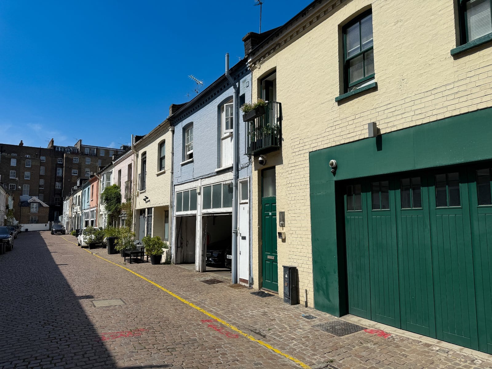 Colourful row of London terraced houses with garage doors on brick-paved street, daytime.