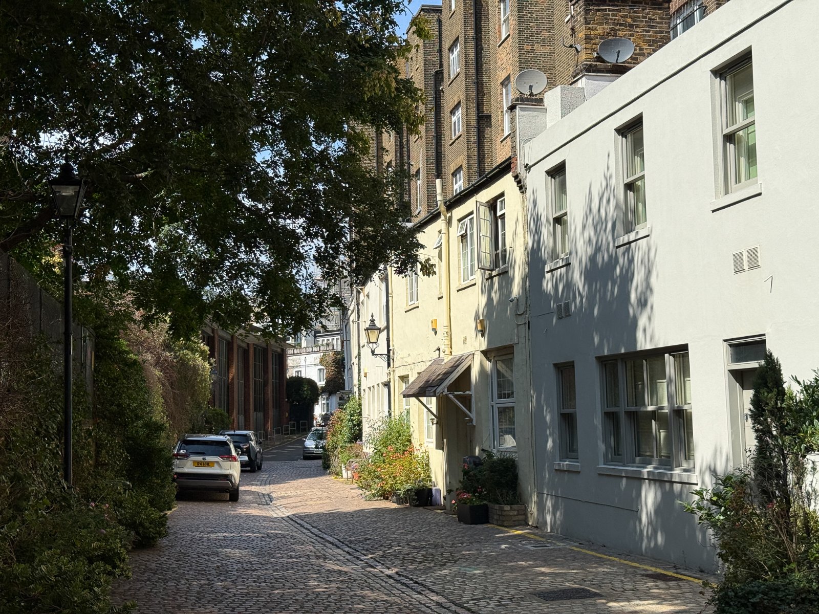 Quaint cobbled street featuring historic terraced homes in London, with lush greenery and charming street lamps.
