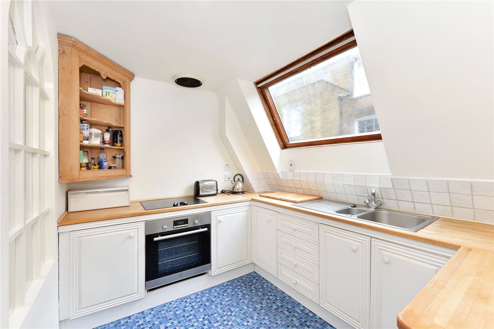 Modern kitchen with white cabinetry and wooden countertops, under a large skylight window.
