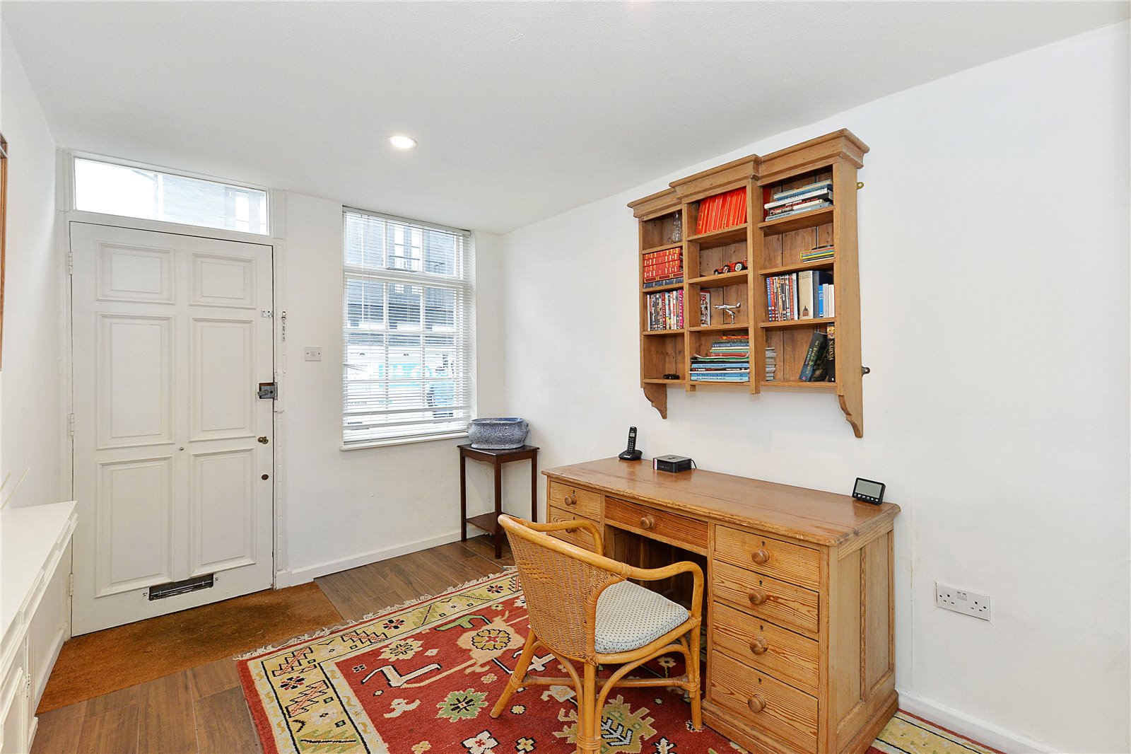 Wooden desk with bookshelves and wicker chair in a bright, modern room with white walls and natural light, featuring classic danish interior style.