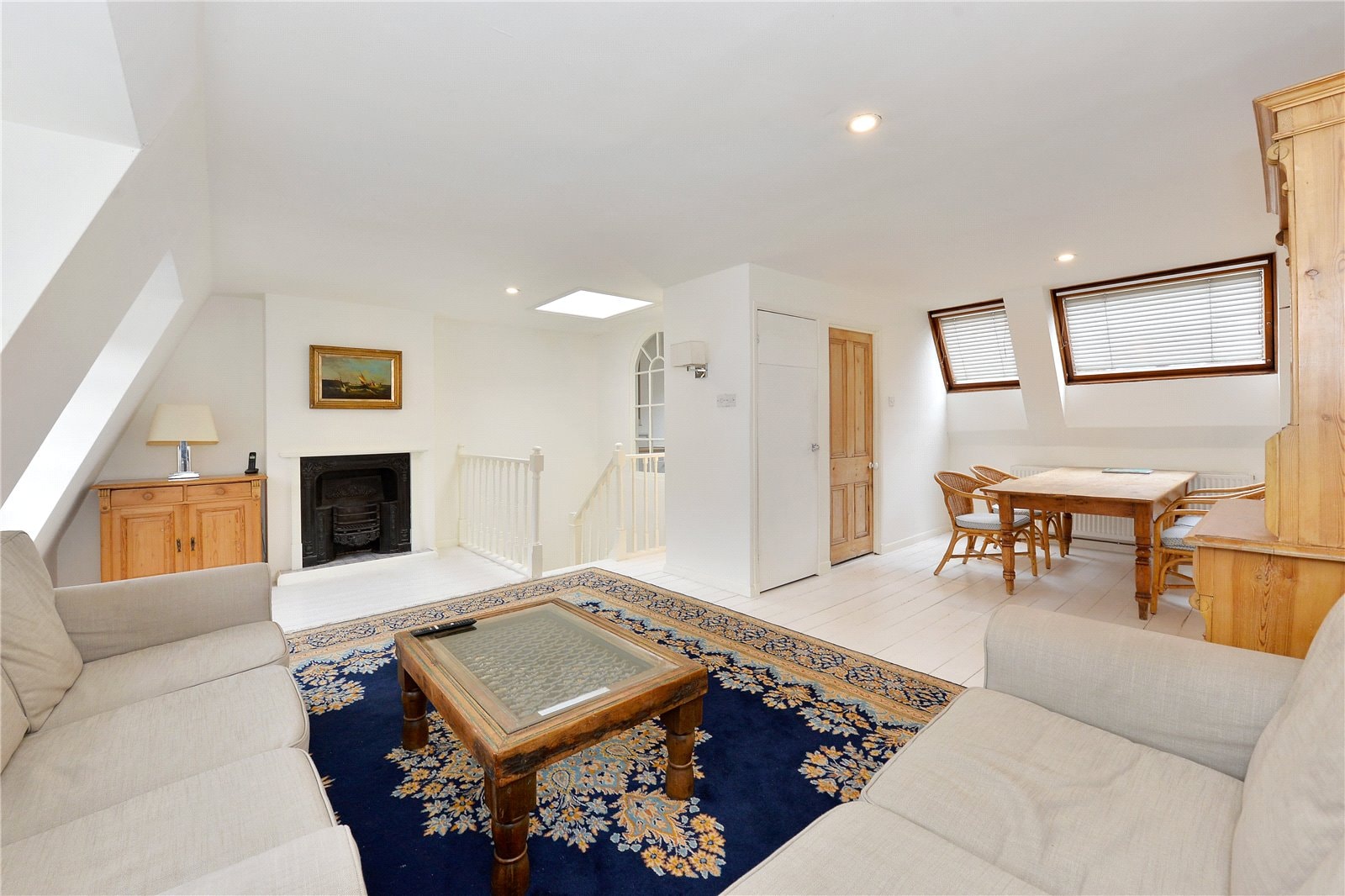 Cozy living room with white walls and wooden accents, skylight, and traditional fireplace. Ideal for stylish London property settings.
