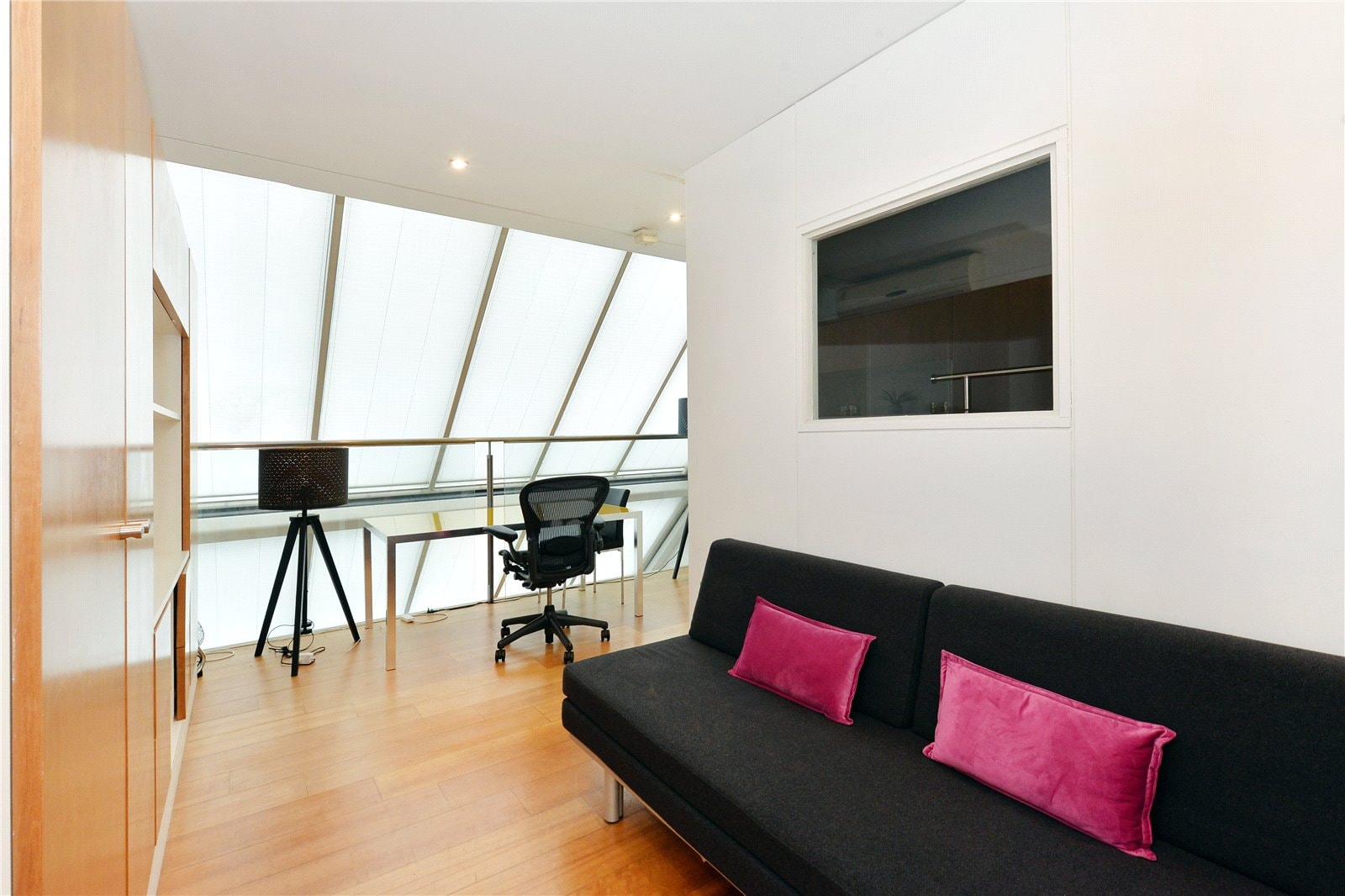 Contemporary loft office with black sofa, pink cushions, and minimalist workspace under skylight.