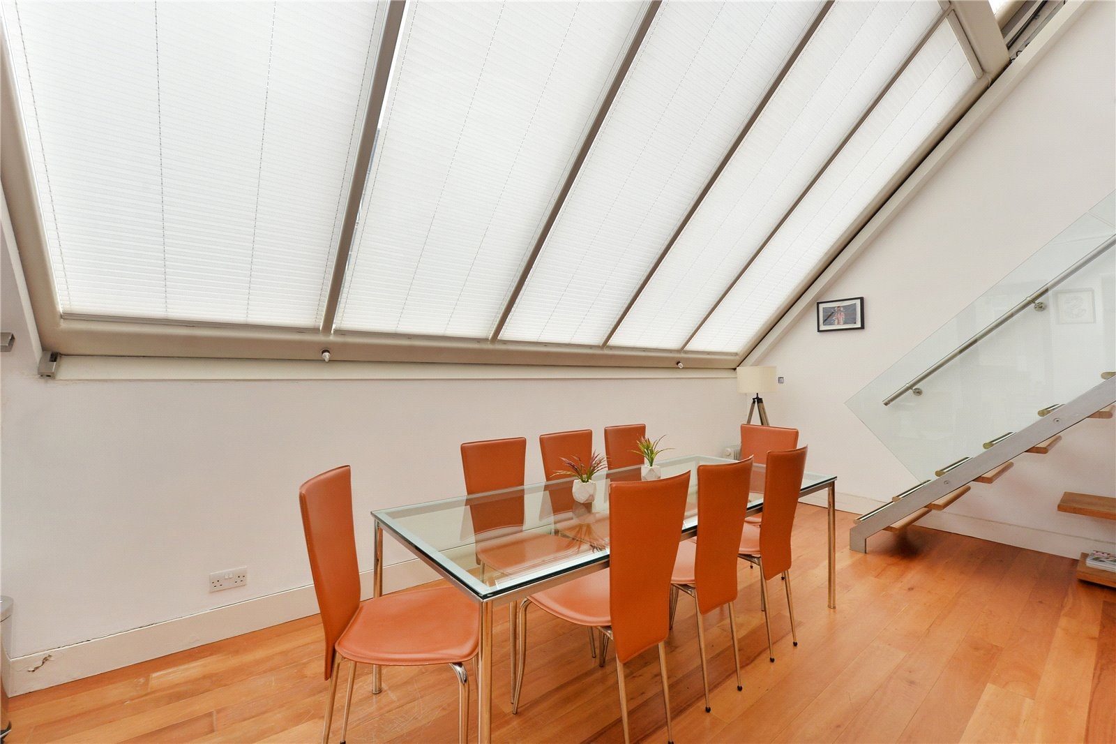 Bright attic dining room with sloped skylight windows and modern orange chairs, featuring wooden flooring and contemporary decor.