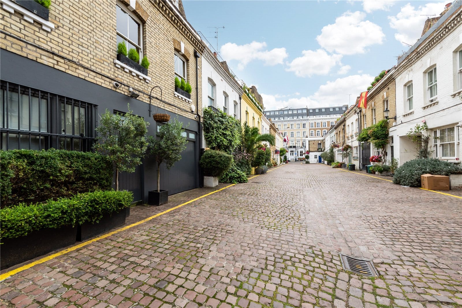 Cobbled street with colourful townhouses, lush plants, and historic architecture in London.