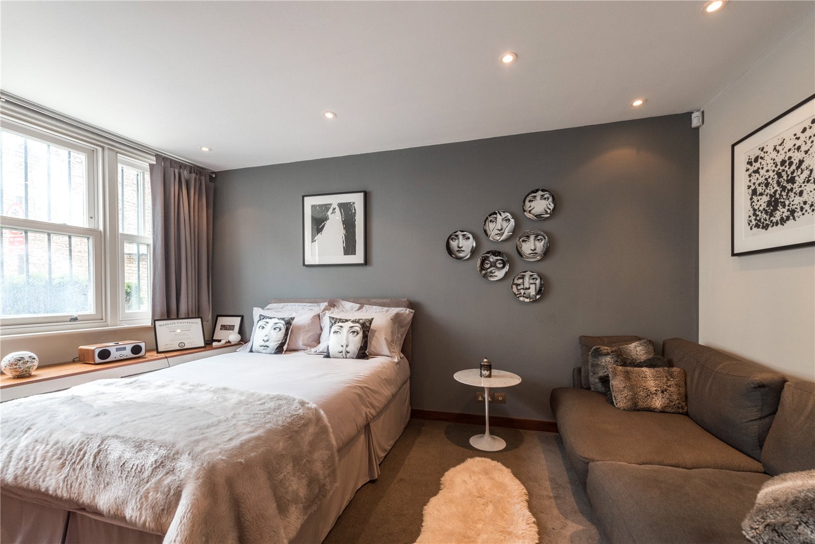 Stylish bedroom with grey accent wall, contemporary art, cosy furnishings, and natural light.