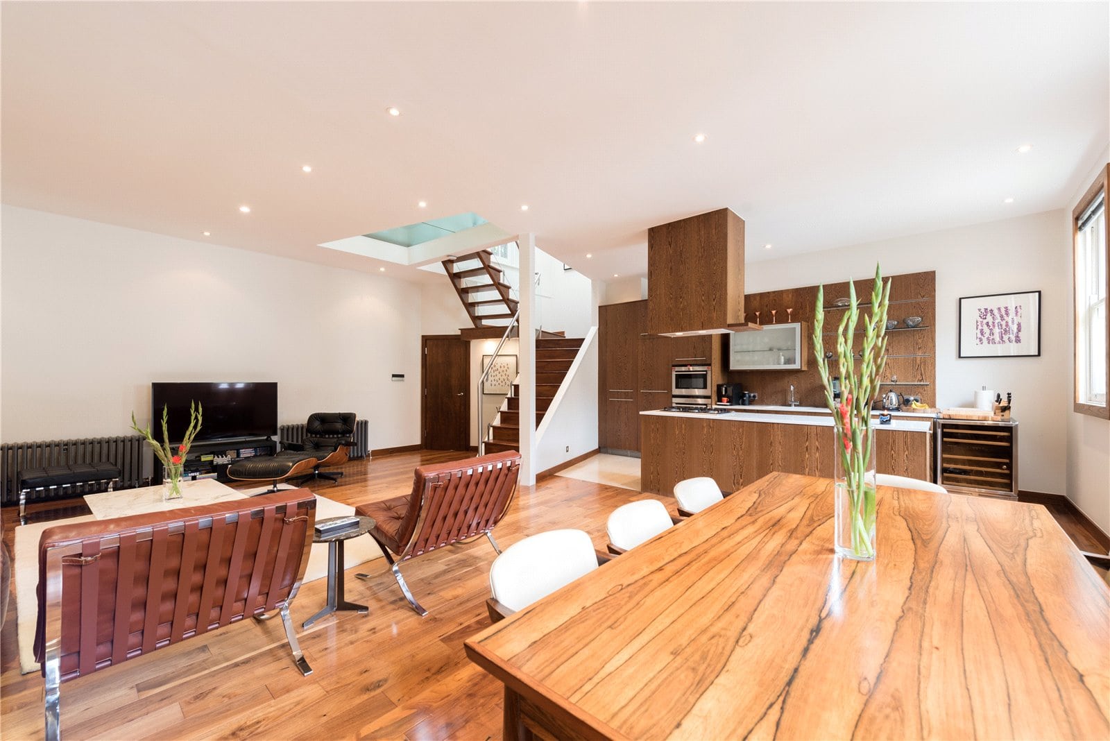 Spacious open-plan living and kitchen area with wooden flooring and modern furnishings, featuring natural light and contemporary design.