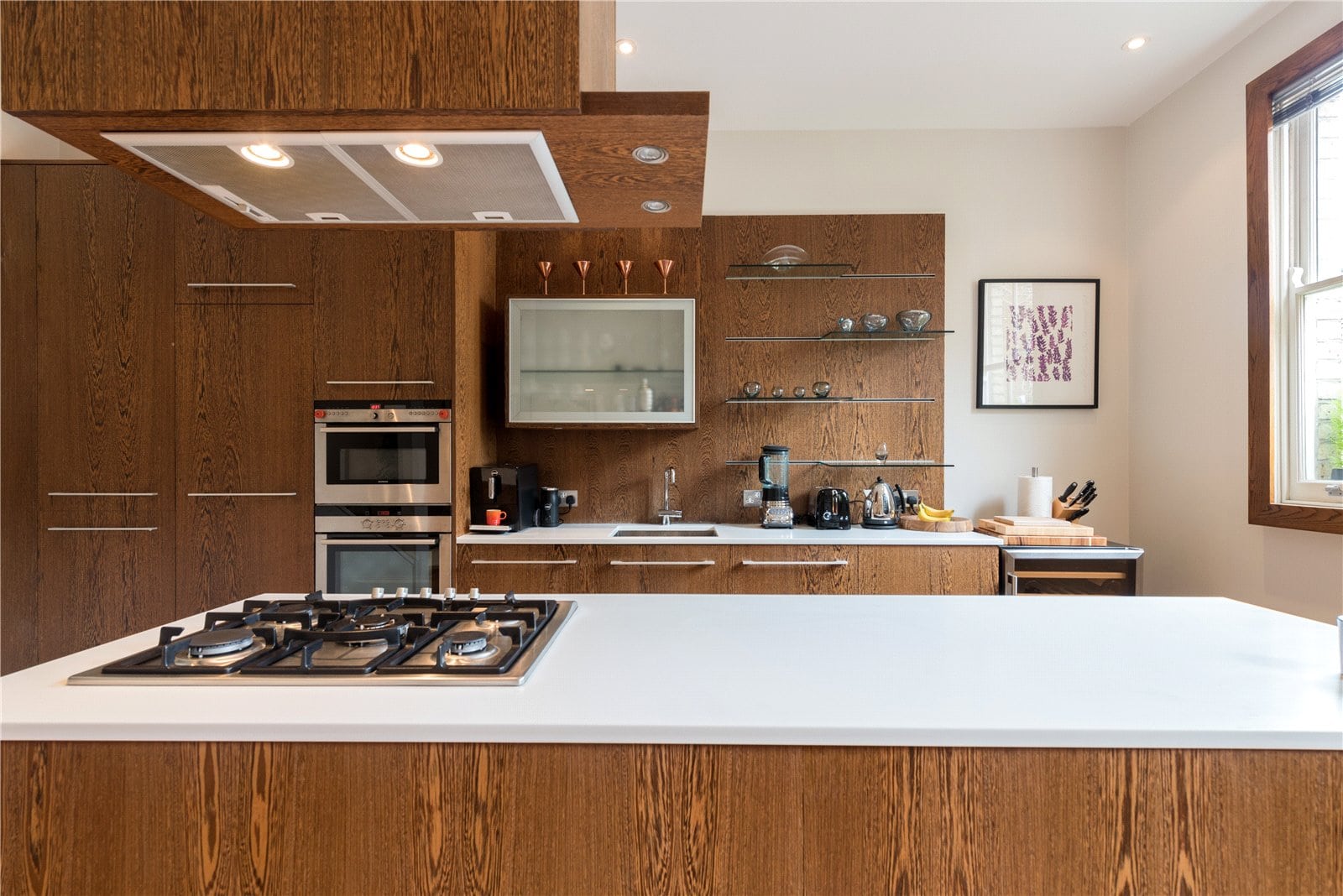Modern kitchen with wooden cabinets and white countertops, featuring built-in appliances and ample natural light.