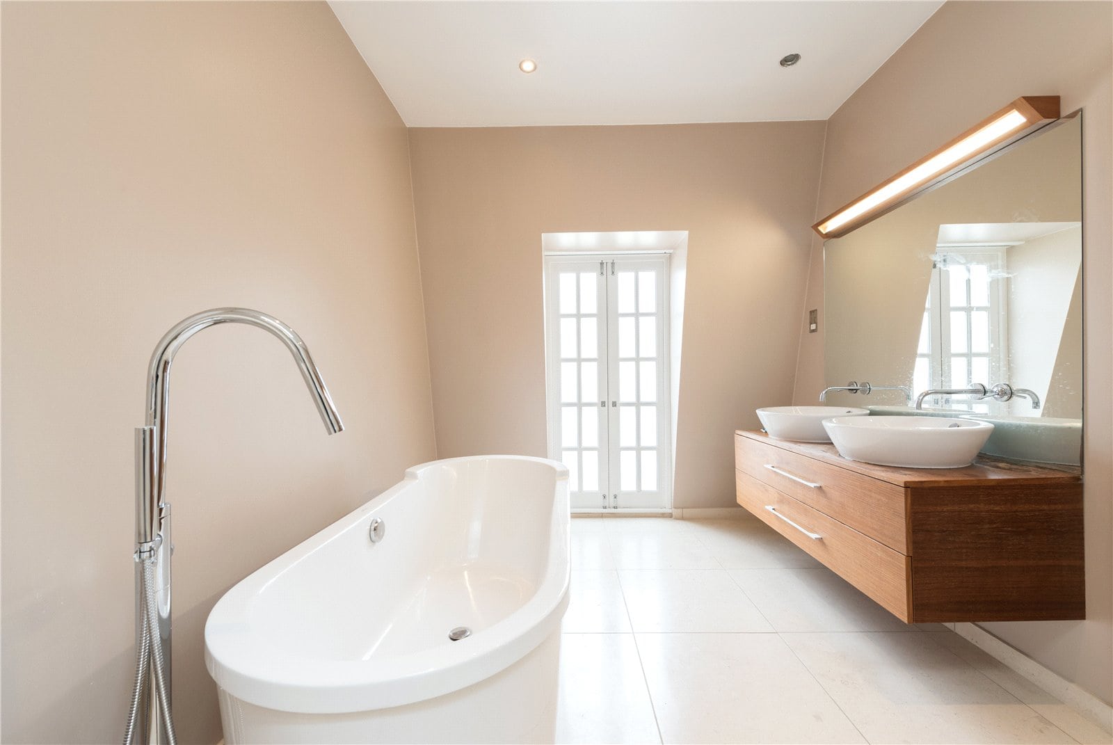 Elegant modern bathroom with white bathtub, dual sinks, and light beige walls, showcasing minimalist luxury.