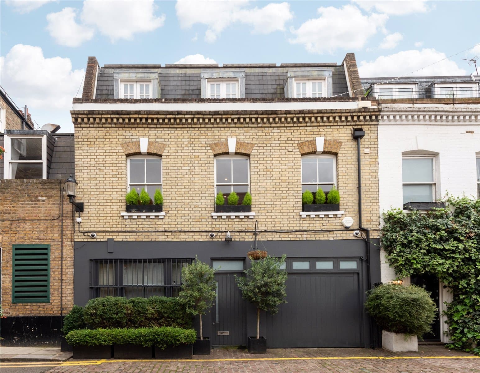 Vintage brick townhouse with modern black garage doors and greenery, centrally located in London.