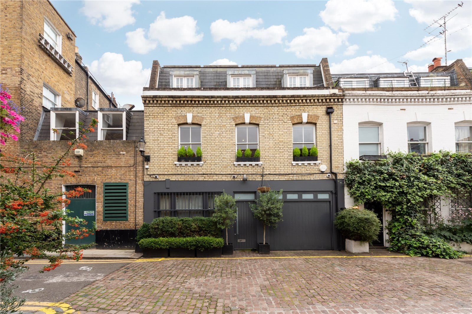 Charming London townhouse with modern black garage door and lush greenery, eco-friendly planters for sale.