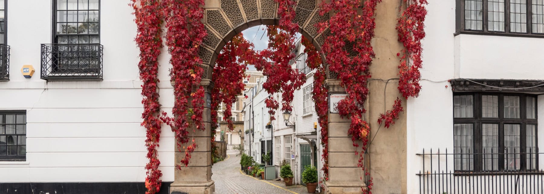 Vibrant red ivy covering an ornate archway in a historic London street scene.