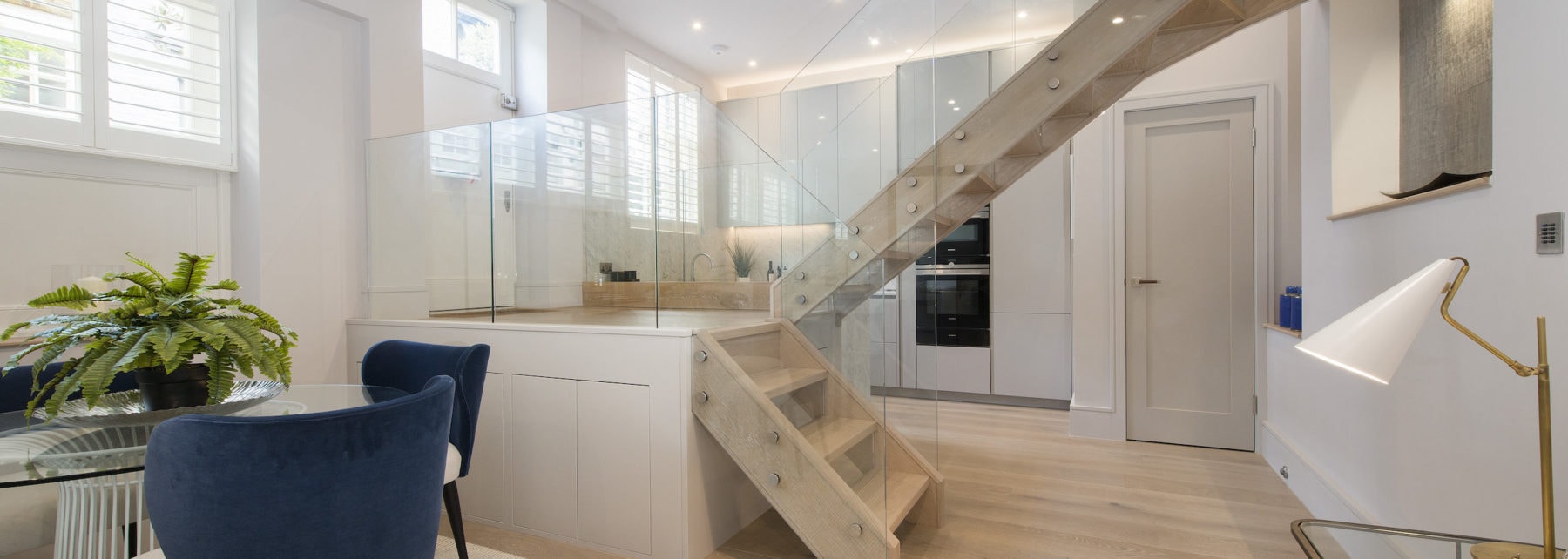 Contemporary open-plan living space with minimalist kitchen and wooden staircase, bright natural light.