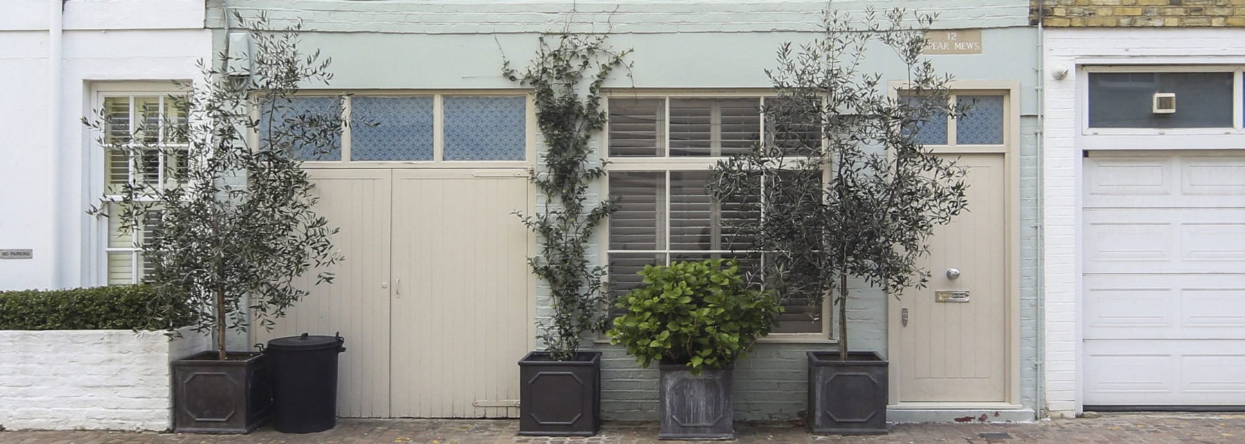 Olive trees in planters outside a city house facade with shutters and brick driveway, urban garden, modern residential exterior design, London living.
