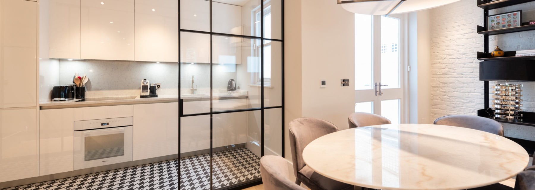 Bright modern kitchen with sleek white cabinetry and a stylish dining area with marble table and velvet chairs.