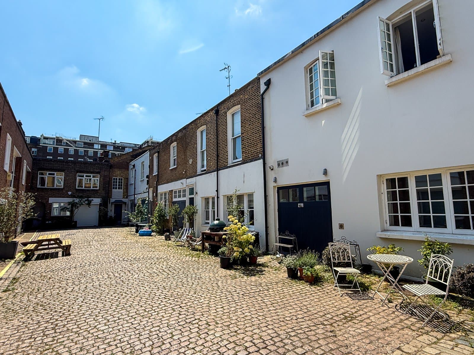 Charming courtyard with cobblestone paving, outdoor seating, and potted plants in London townhouse garden.