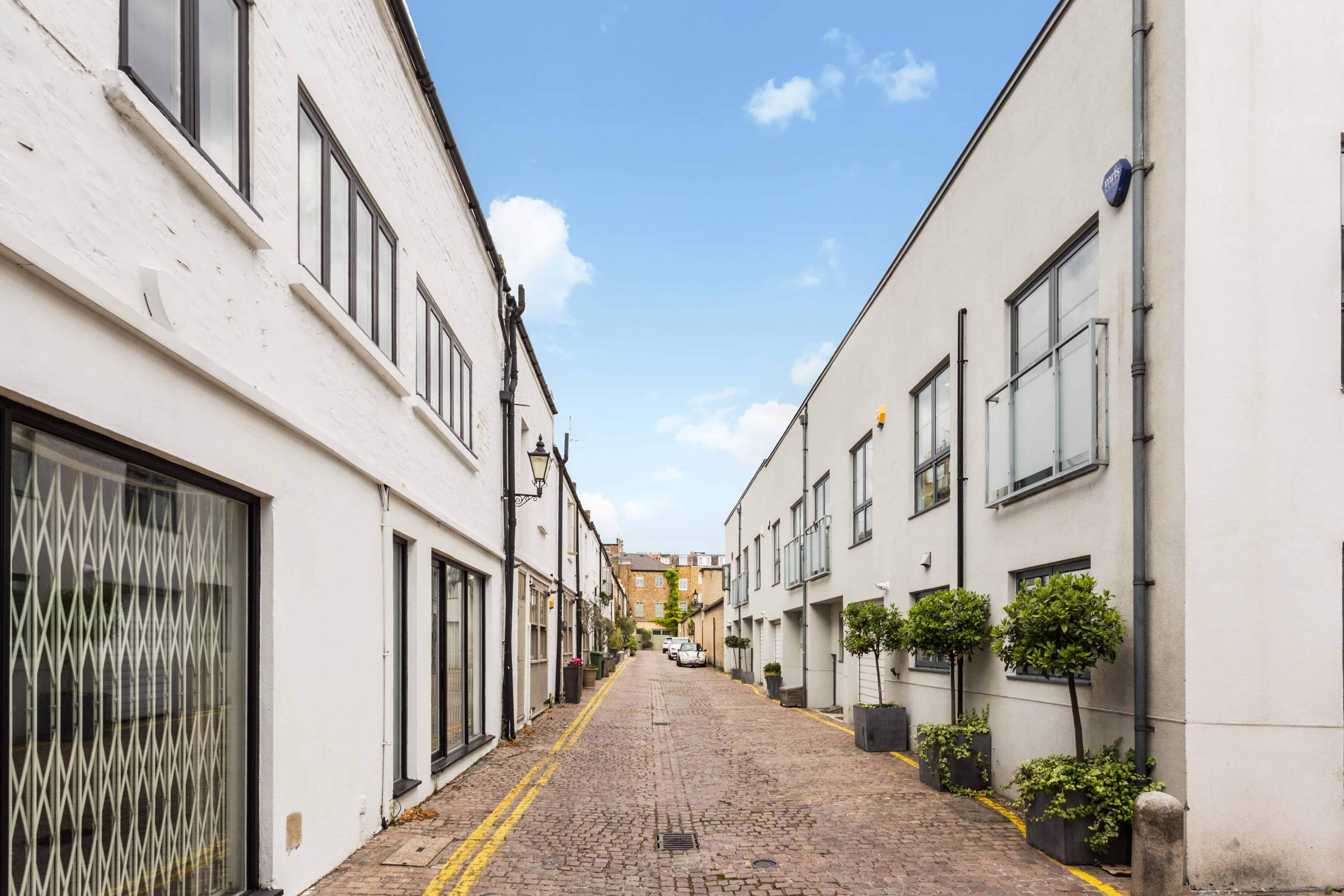 Quiet cobbled street with white modern houses and potted plants in a London mews.