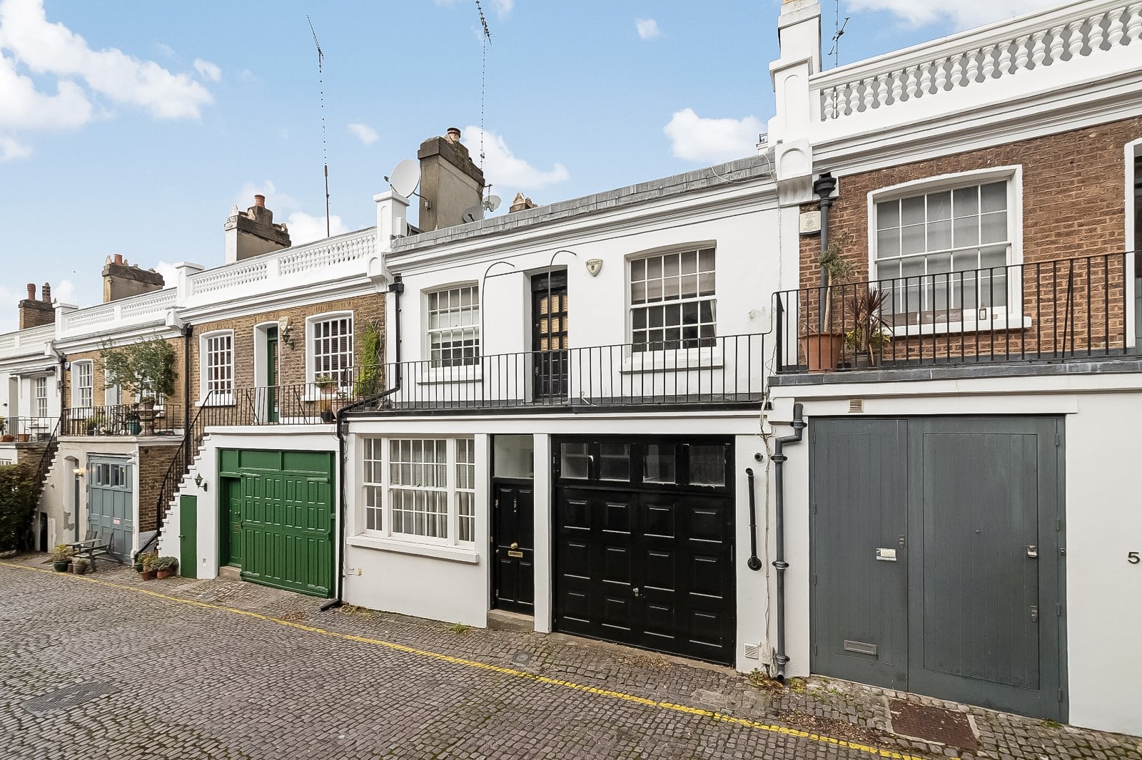 Charming terraced houses in London with colourful garage doors and black railings, showcasing classic Victorian architecture.