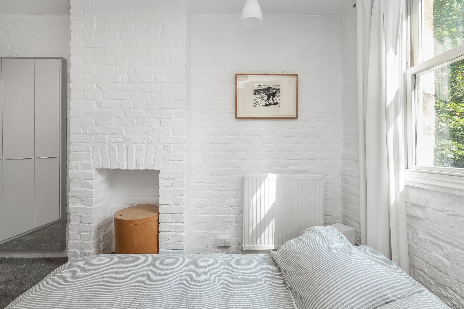 Cozy white bedroom with brick walls, large window, and minimalist decor.