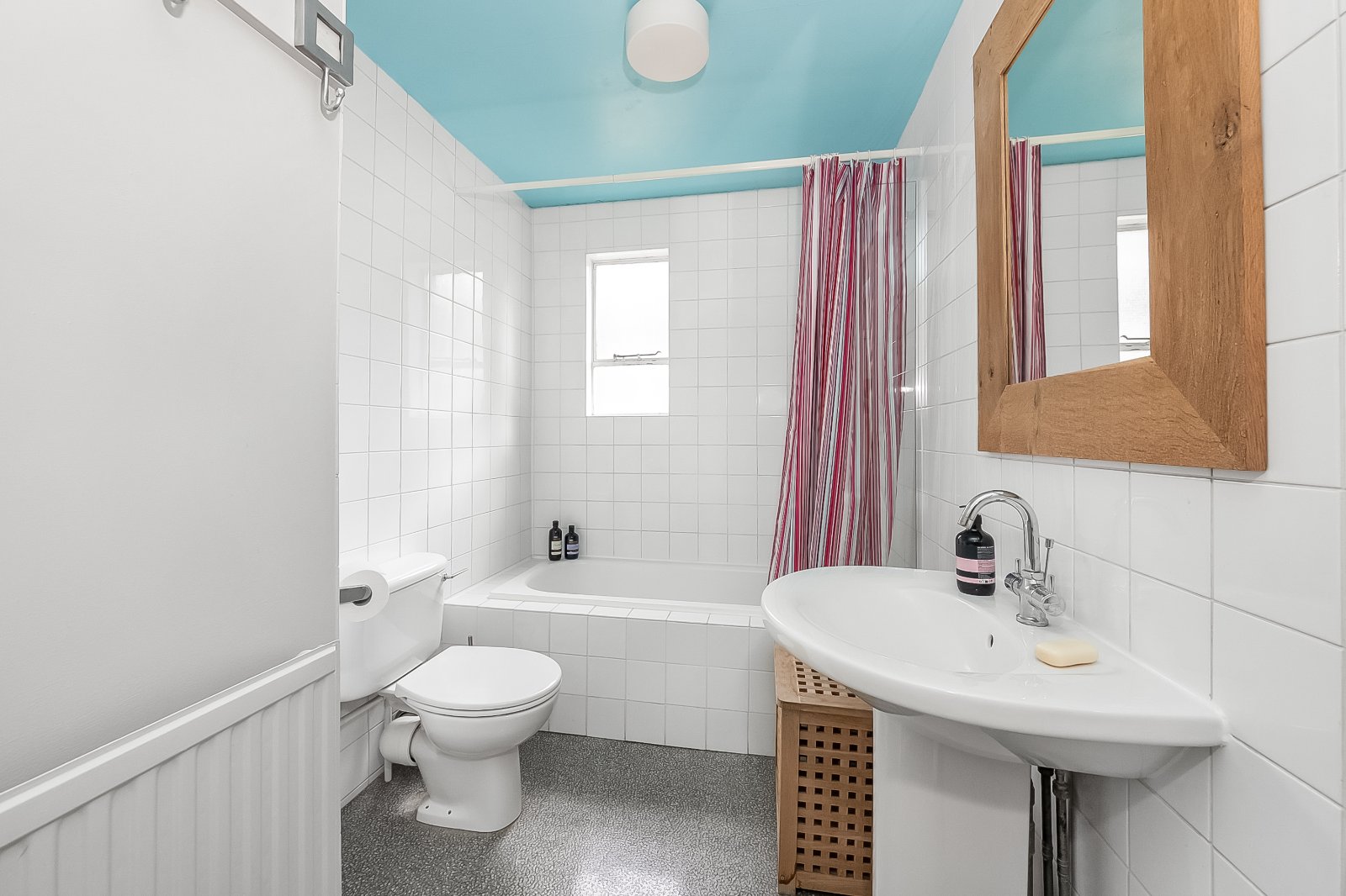 Bright bathroom with white tiles, blue ceiling, and natural wood accents at Lurot Brand.
