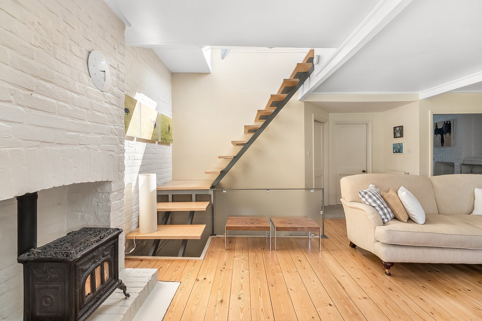 Bright living room featuring modern staircase, cream sofa, and cosy fireplace with rustic decor.
