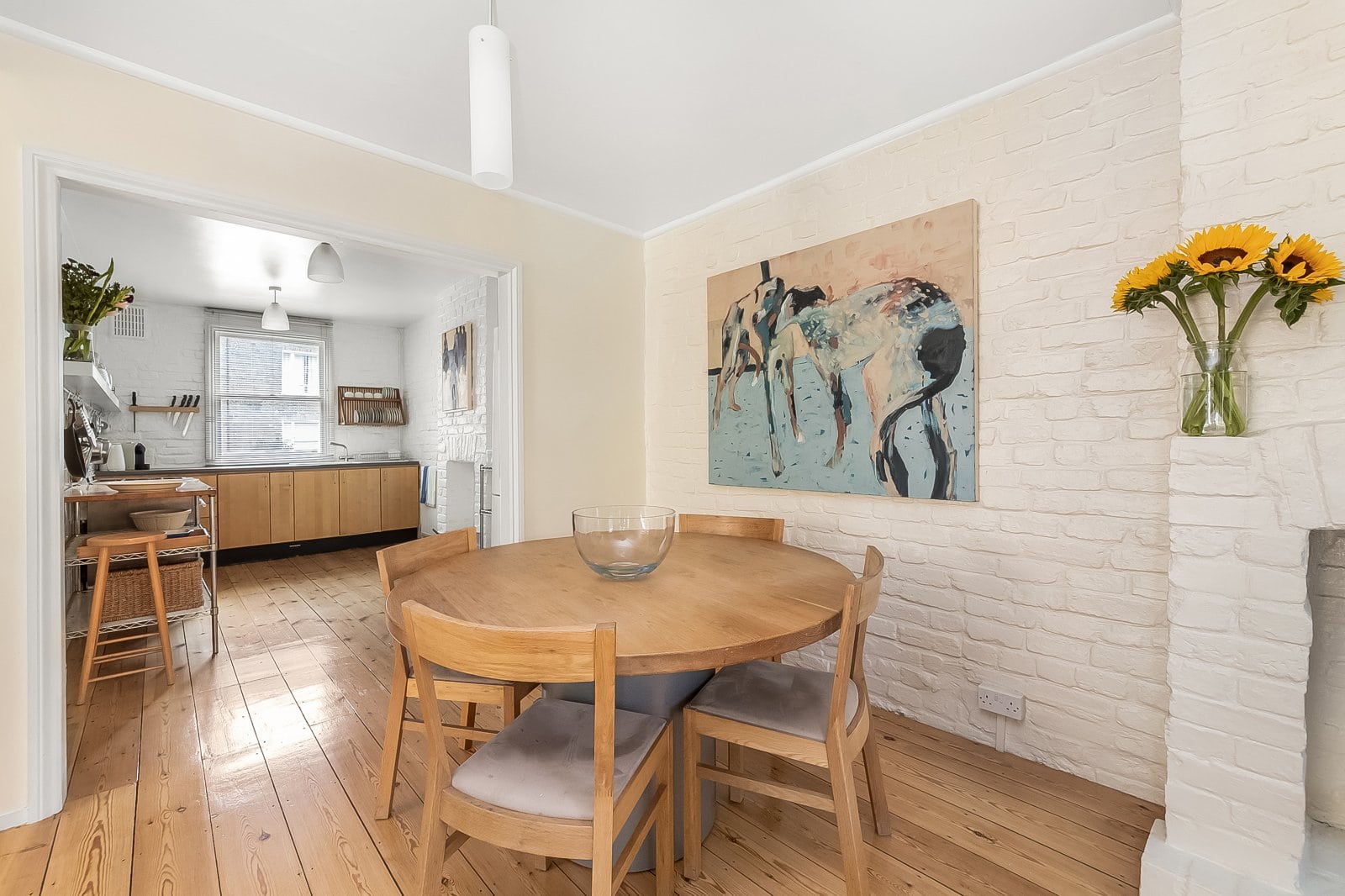 Bright dining area with white brick wall, wooden table and sunflower vase, showcasing stylish interior design by Lurot Brand.