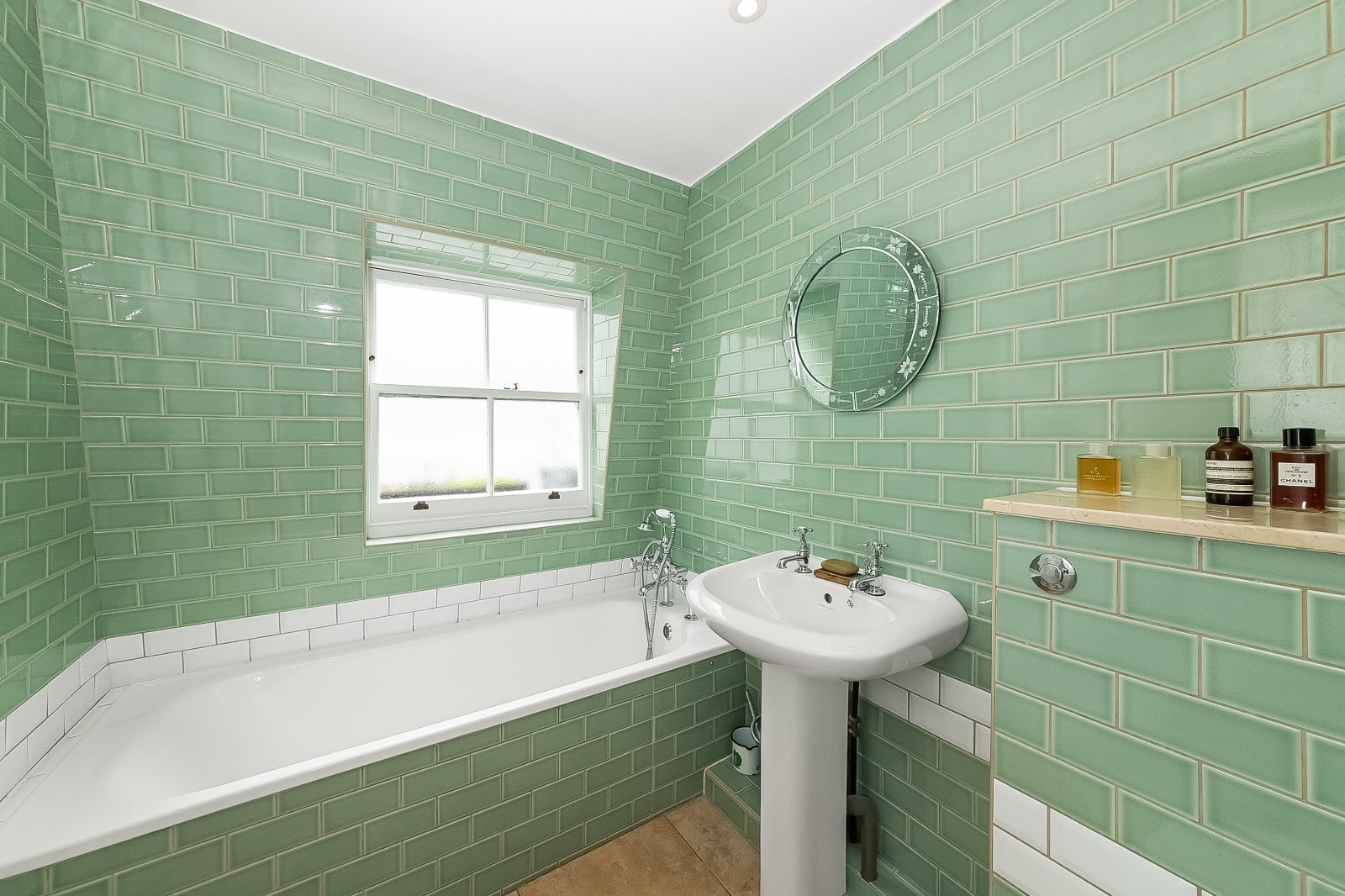 Bright green tiled bathroom with vintage bathtub and pedestal sink, stylish decor, natural light, and characterful design.
