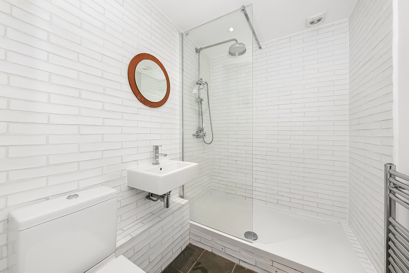 Modern white brick bathroom with walk-in shower, small sink, and heated towel rail. Stylish and functional space.
