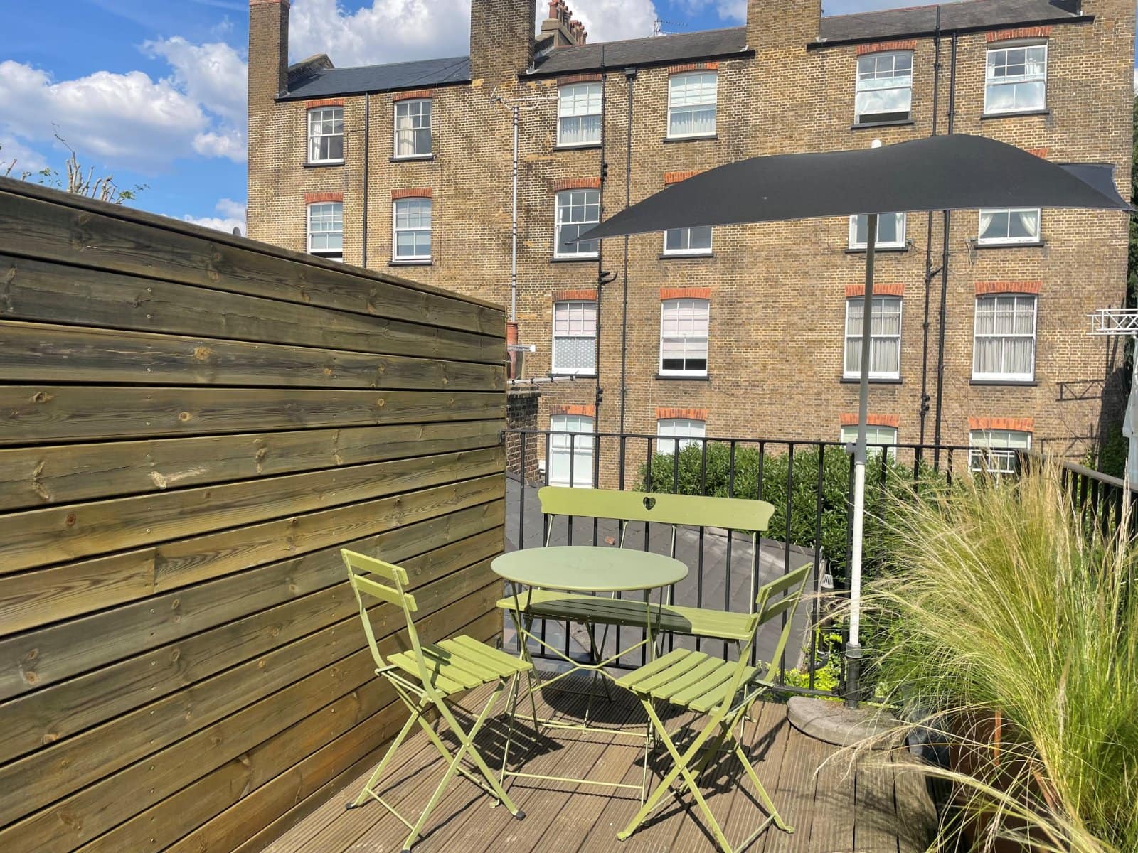 Cozy London rooftop terrace with outdoor furniture and large umbrella overlooking historic brick buildings.