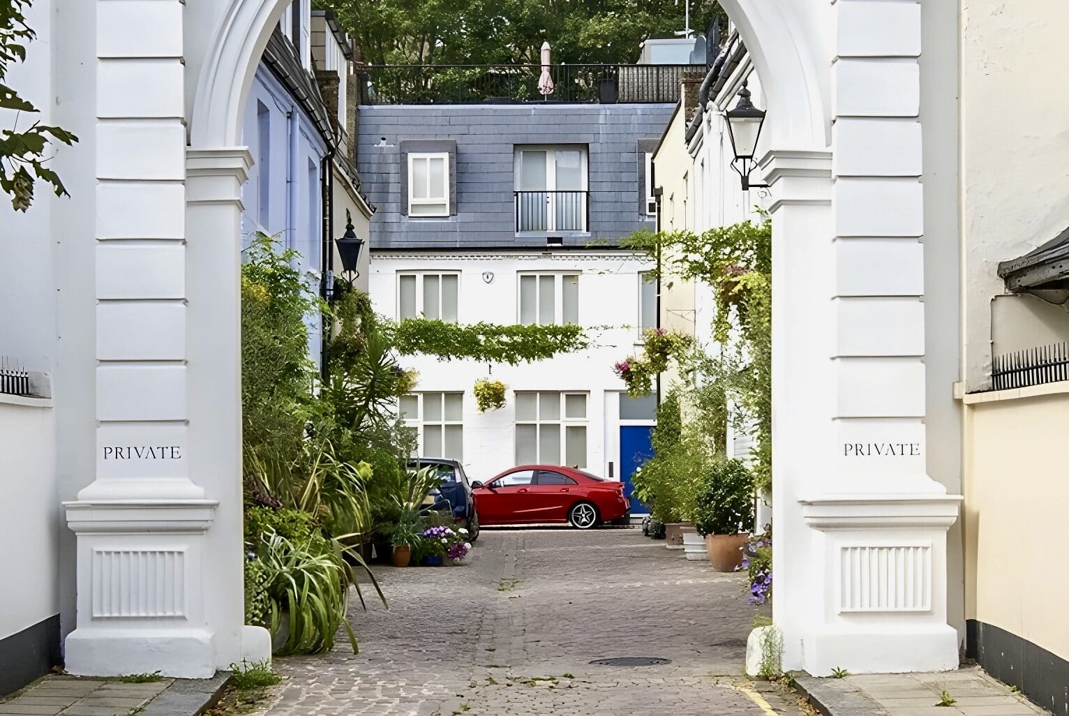 Spacious private courtyard with lush plants, classic architecture, and a red car in central London.