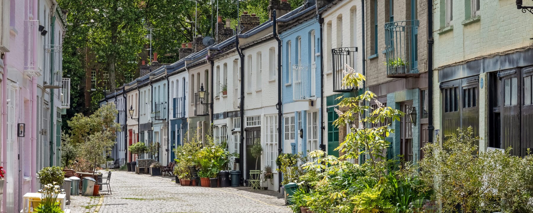 Colourful cobbled street with charming pastel terrace houses in Notting Hill, London, featuring vibrant facades and lush greenery.