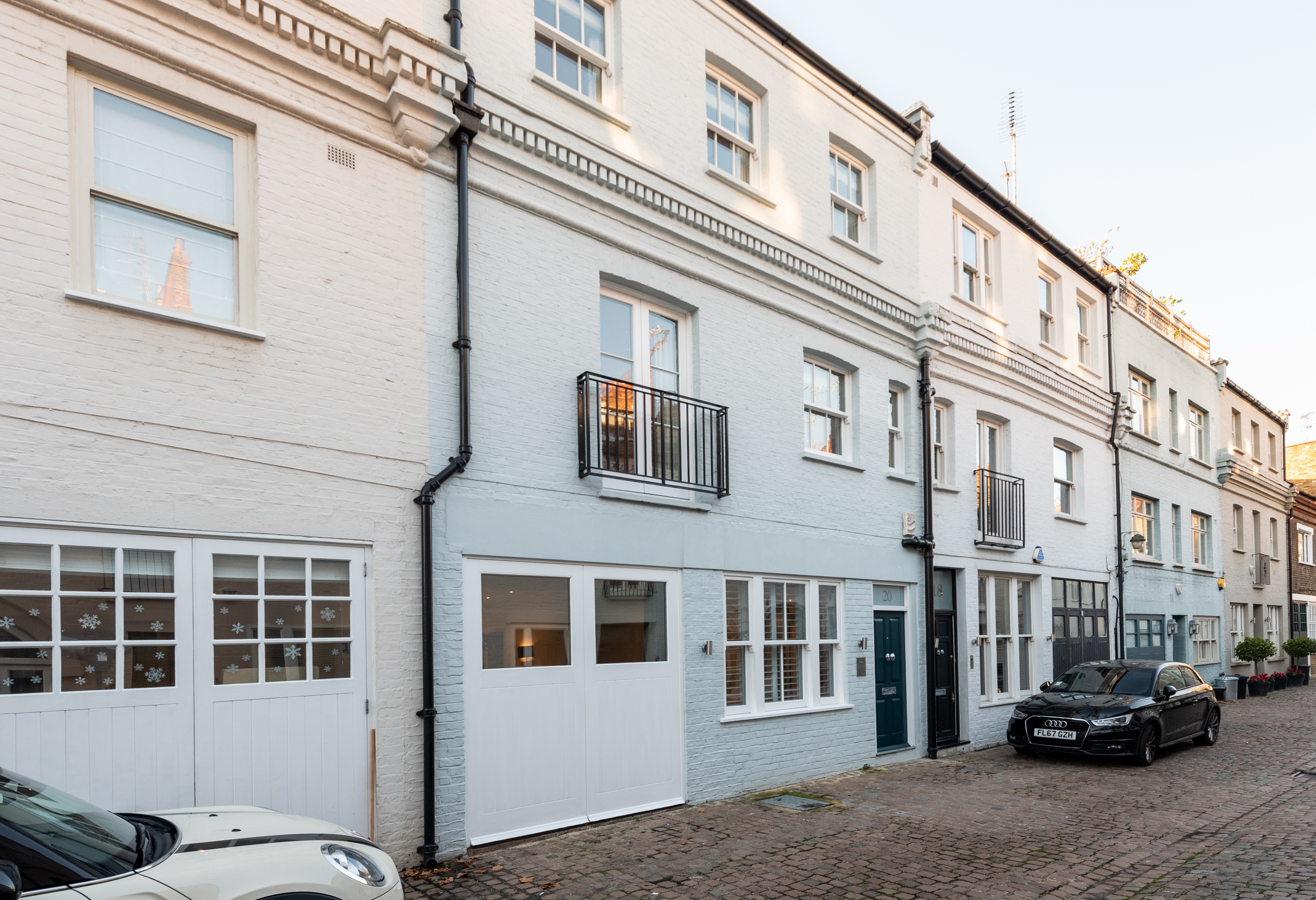 A blue mews house in a mews street with a white garage