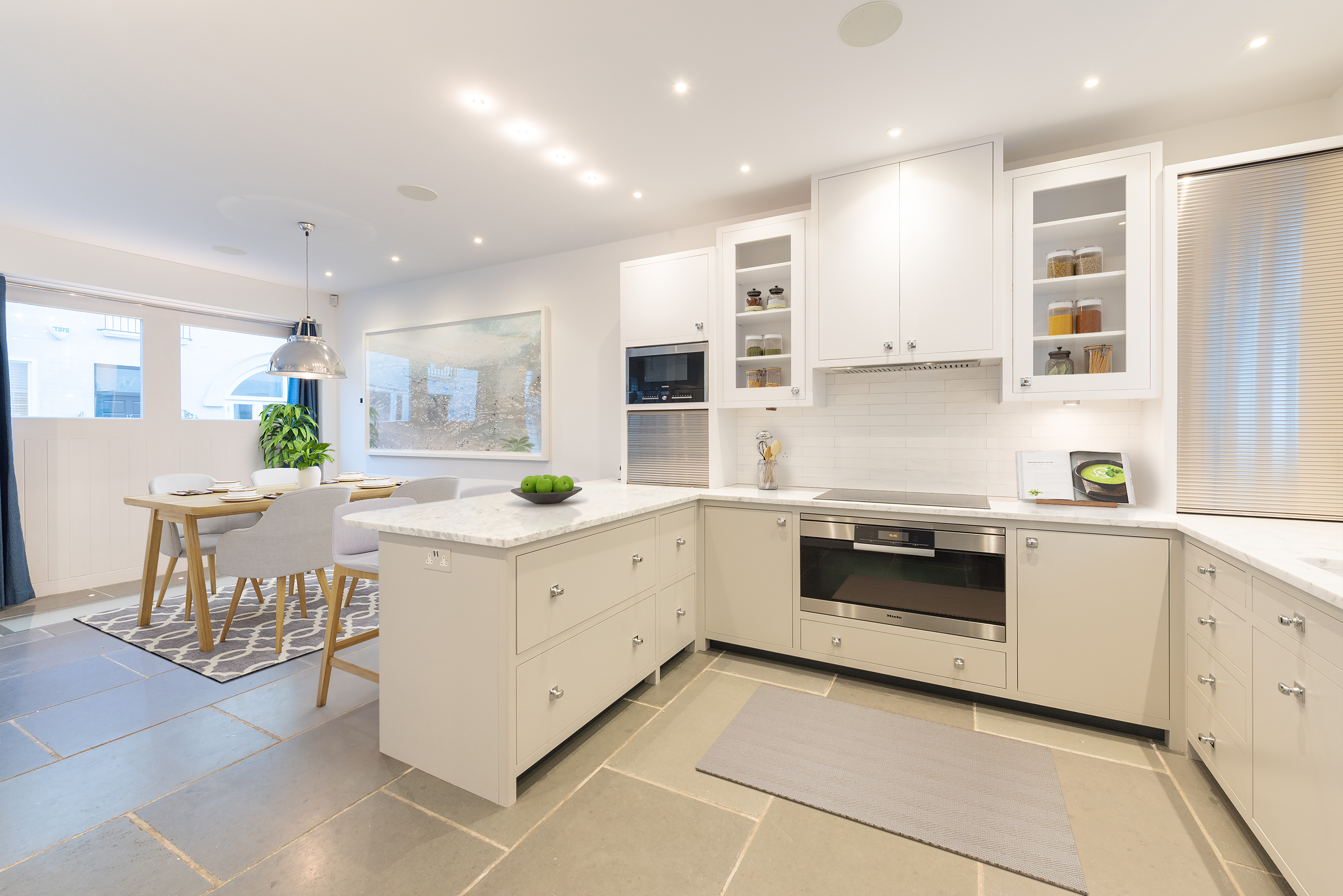 A white open-plan kitchen in a mews property with a dining area with a wooden table and chairs