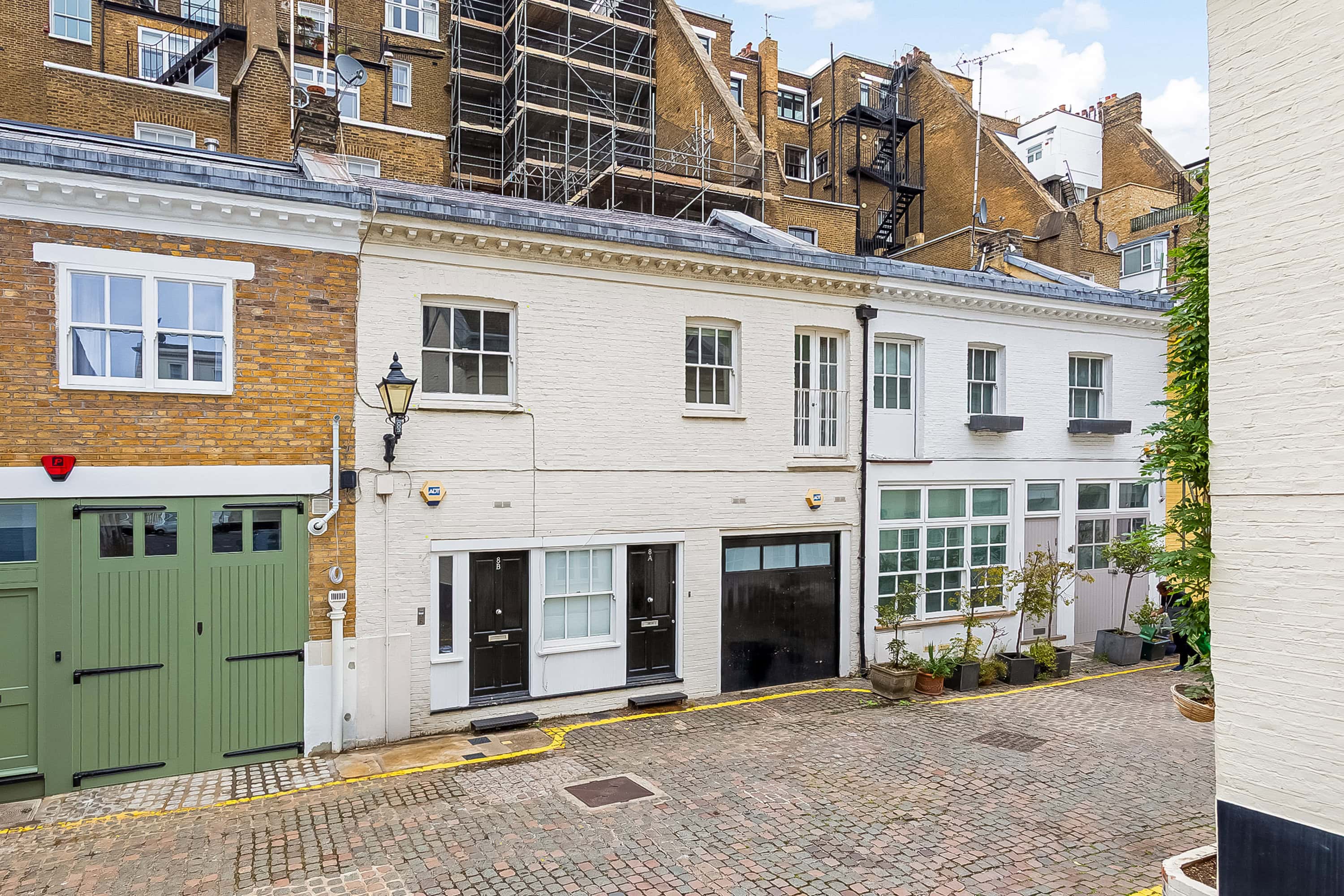 A white property in a mews street with black doors available for sale