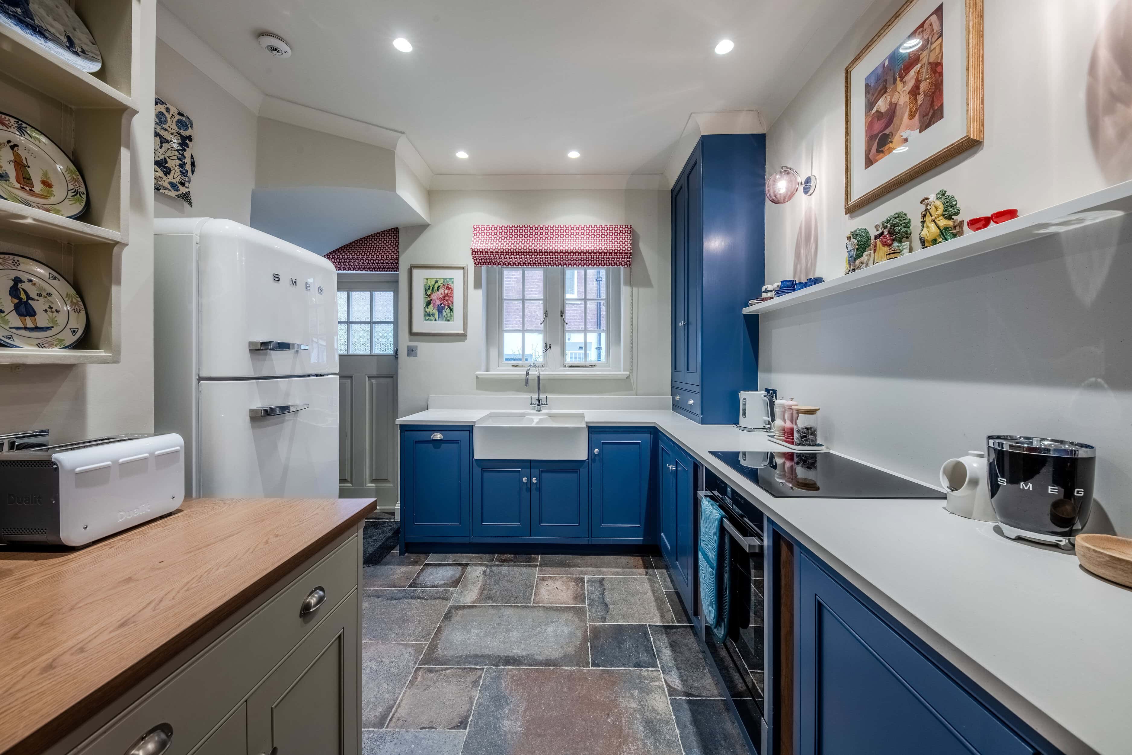 A kitchen with blue cupboards and a fridge in a kitchen in a mews property