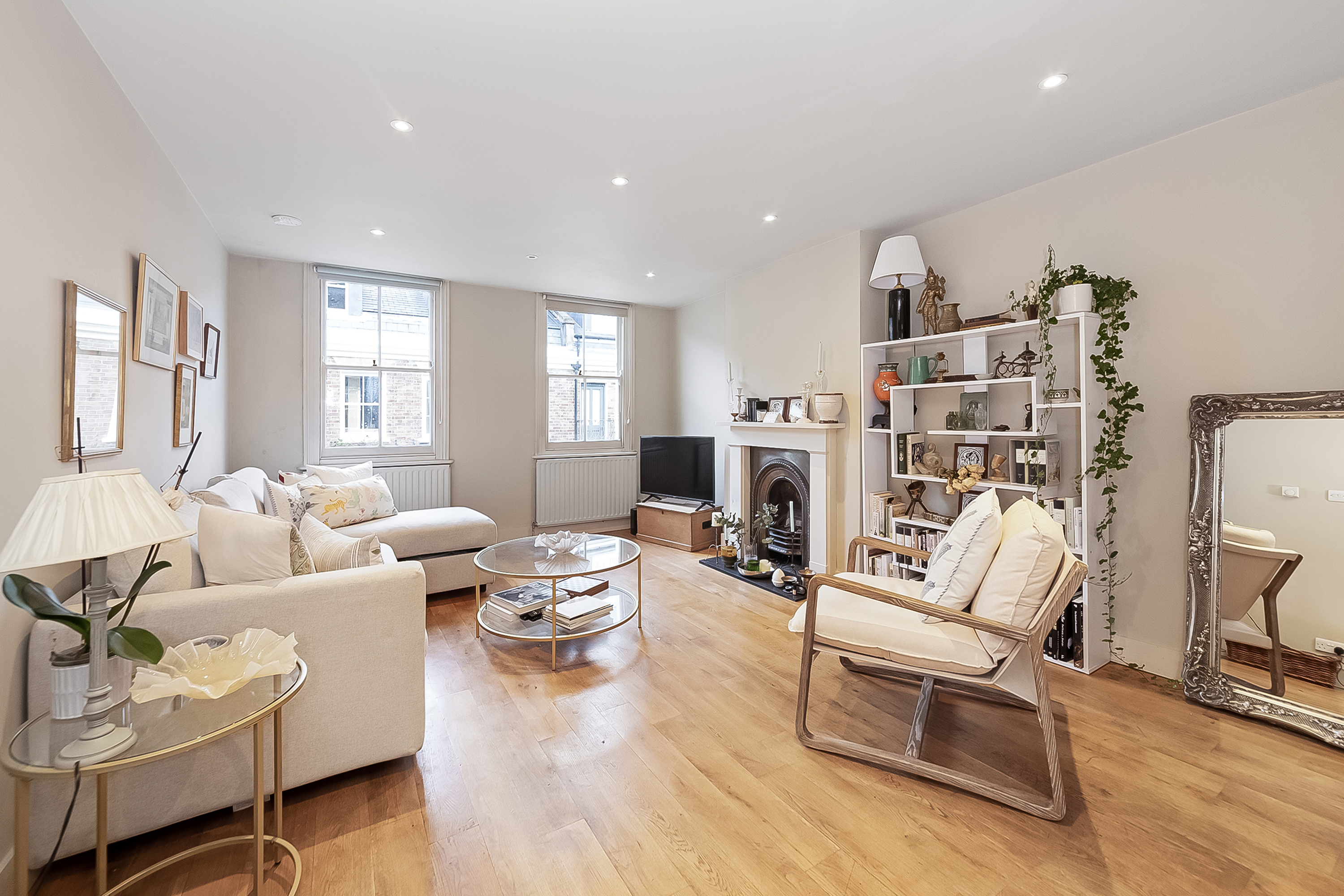 A cream reception room with an arm chair, sofa, shelves and a television in a mews property