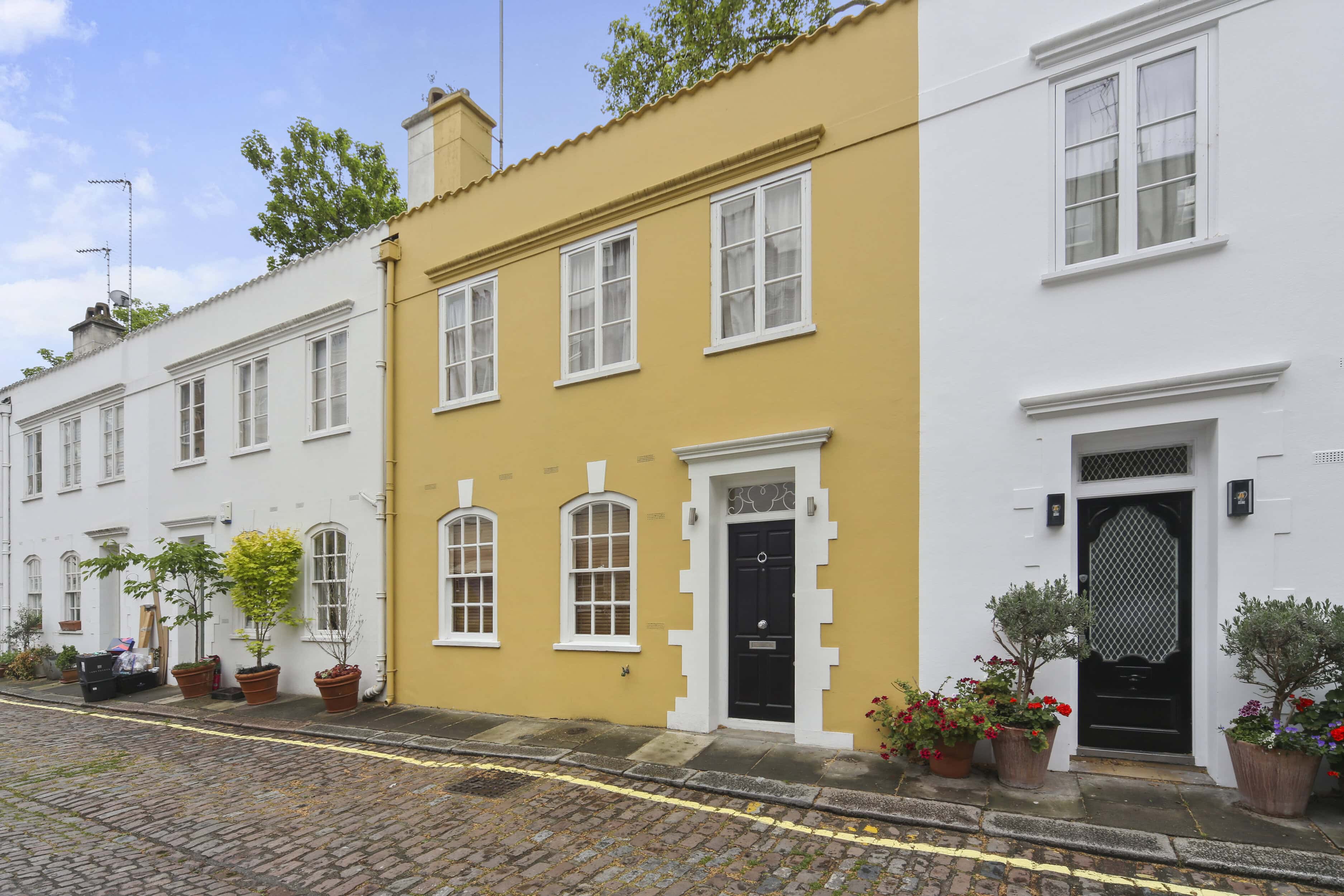 A yellow mews house on a cobbled mews street with two white mews houses