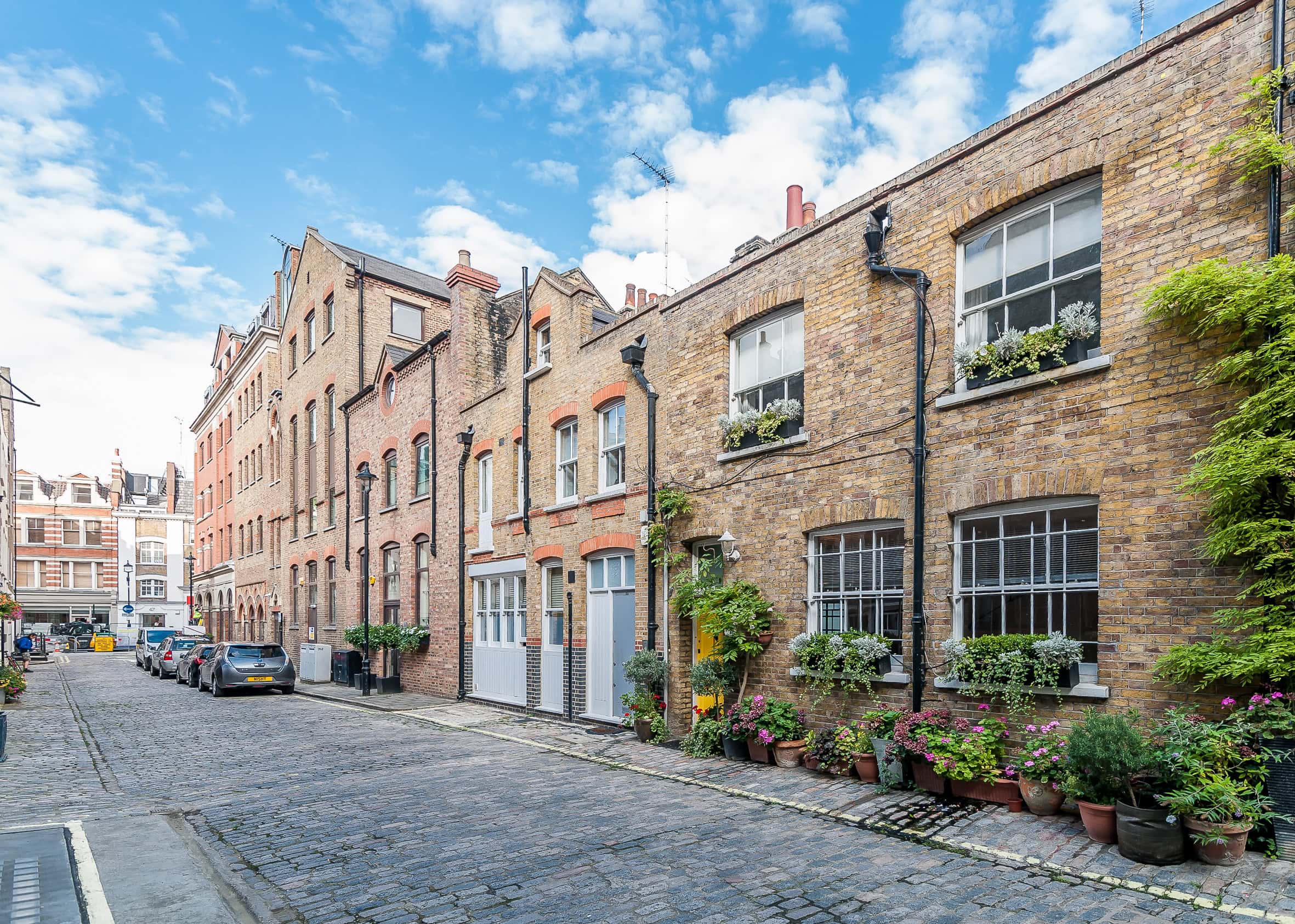 Lurot Brand, charming cobbled street with historic brick houses and lush greenery in London.
